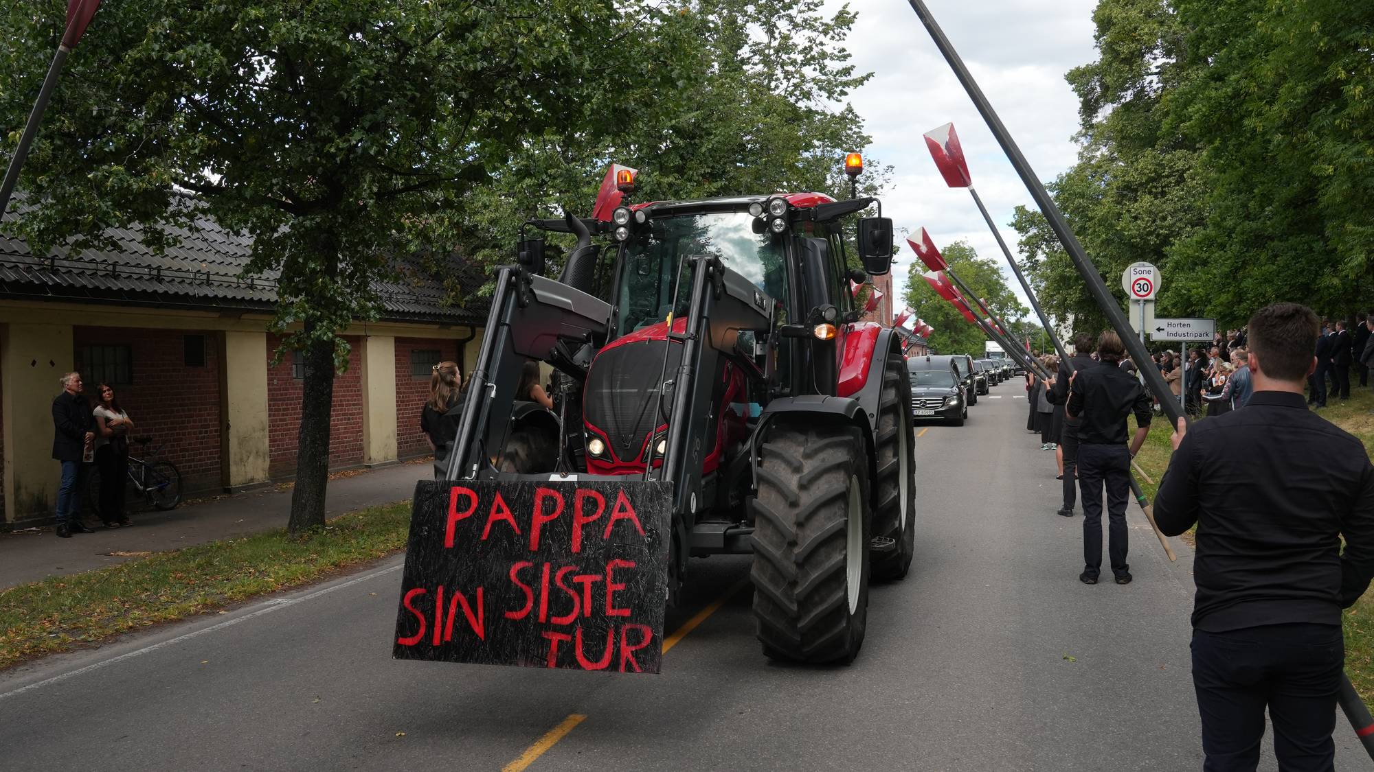 Traktor med skiltet «Pappa sin siste tur» leder et gravfølge med sørgende som holder årer.