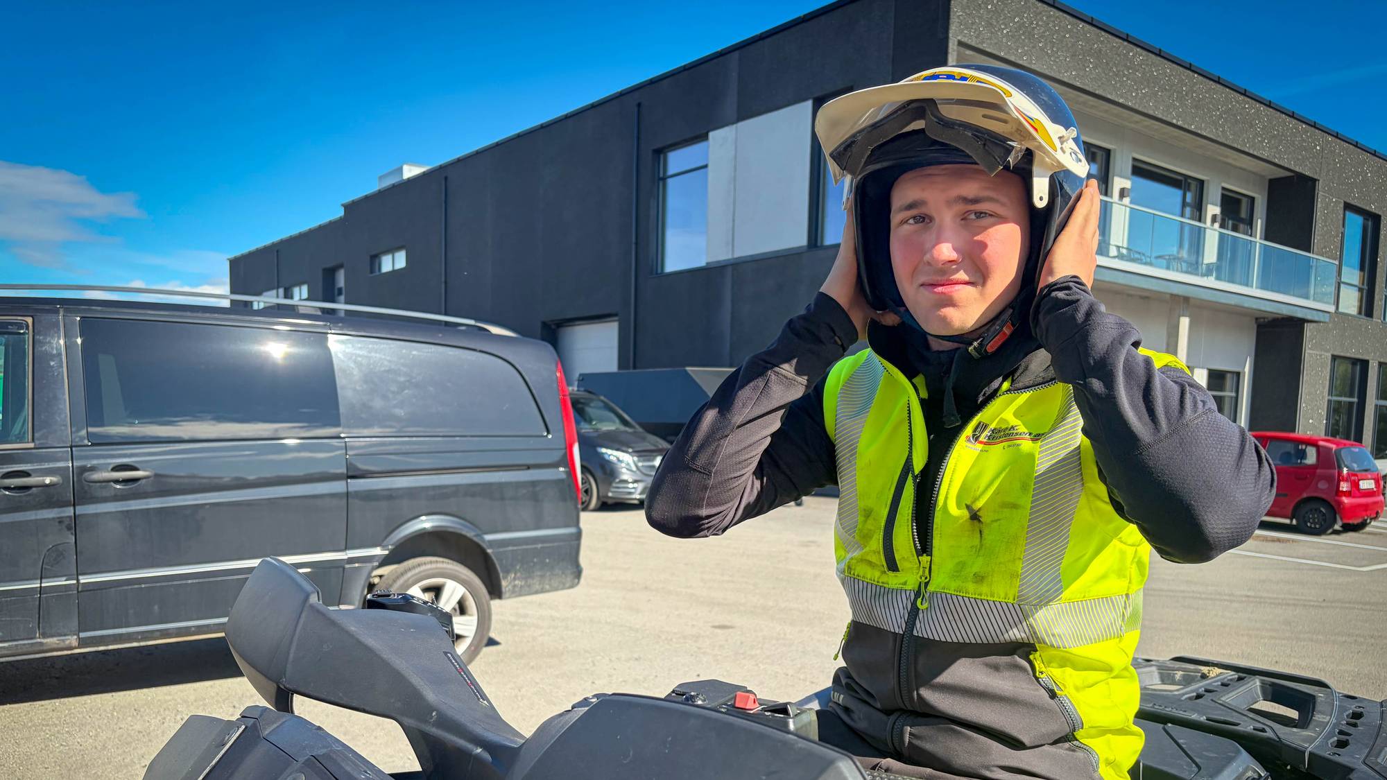 En ung gutt som tar hjelmen på seg mns han sitter på en firehjuling. 