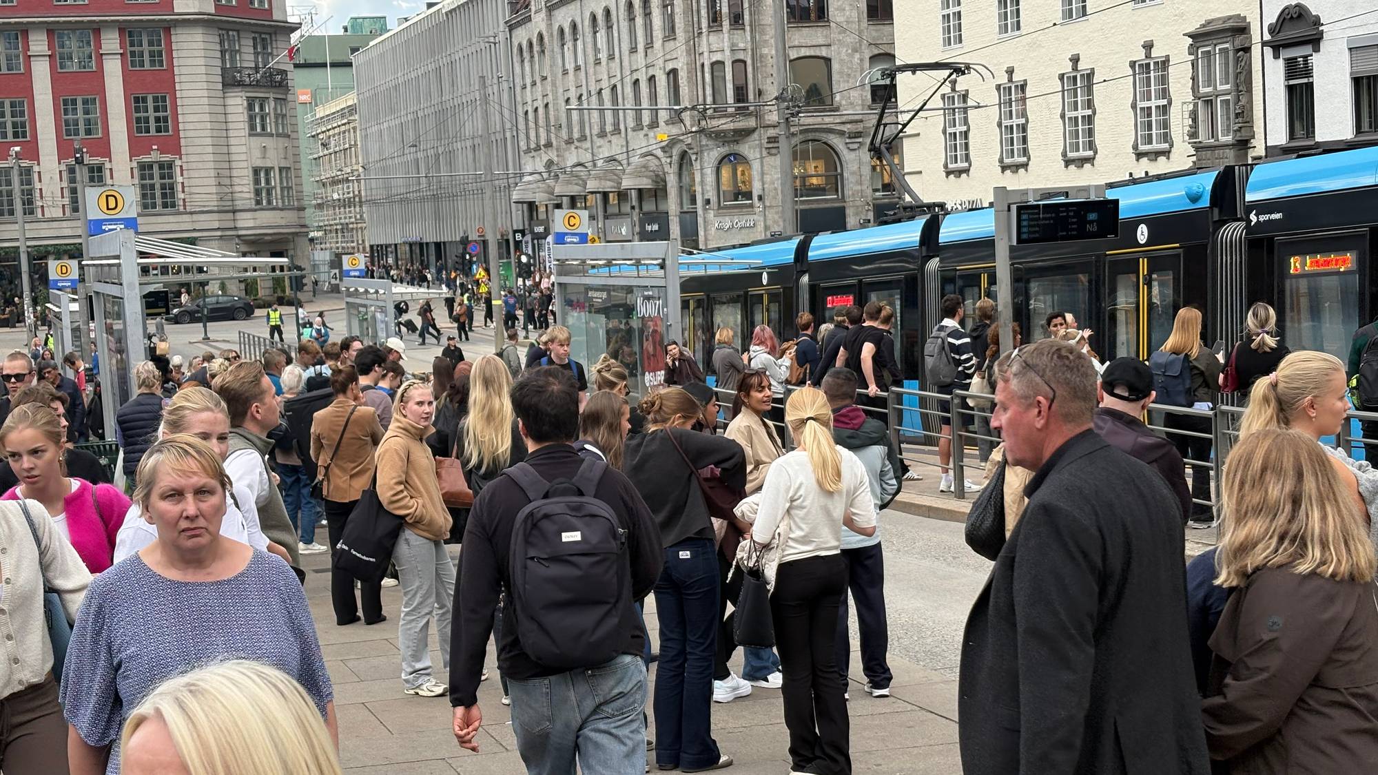 Folk venter på trikken ved et travelt bystopp i Oslo sentrum. (Bildebeskrivelsen er laget av en KI-tjeneste)