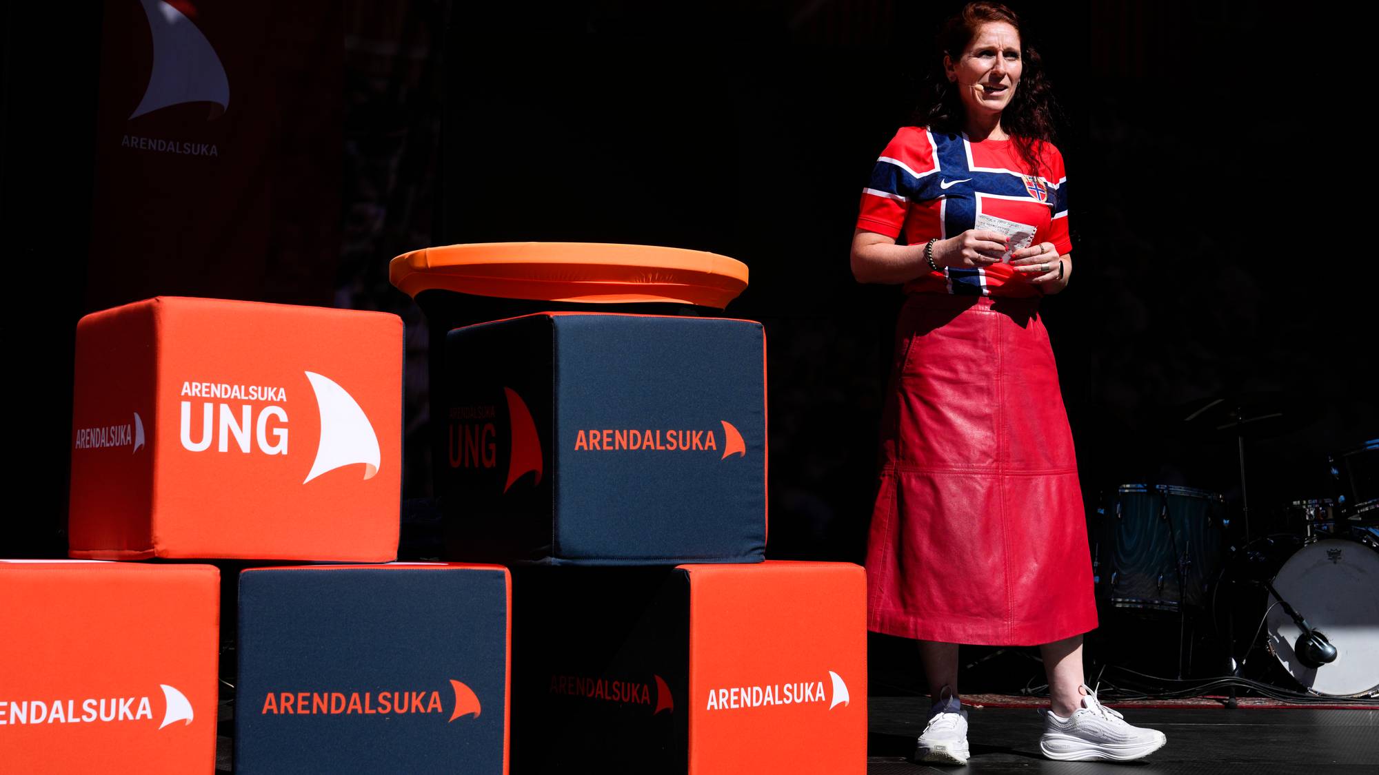 Kvinne i norgesdrakt holder tale på en scene med Arendalsuka-logoer. (Bildebeskrivelsen er laget av en KI-tjeneste)