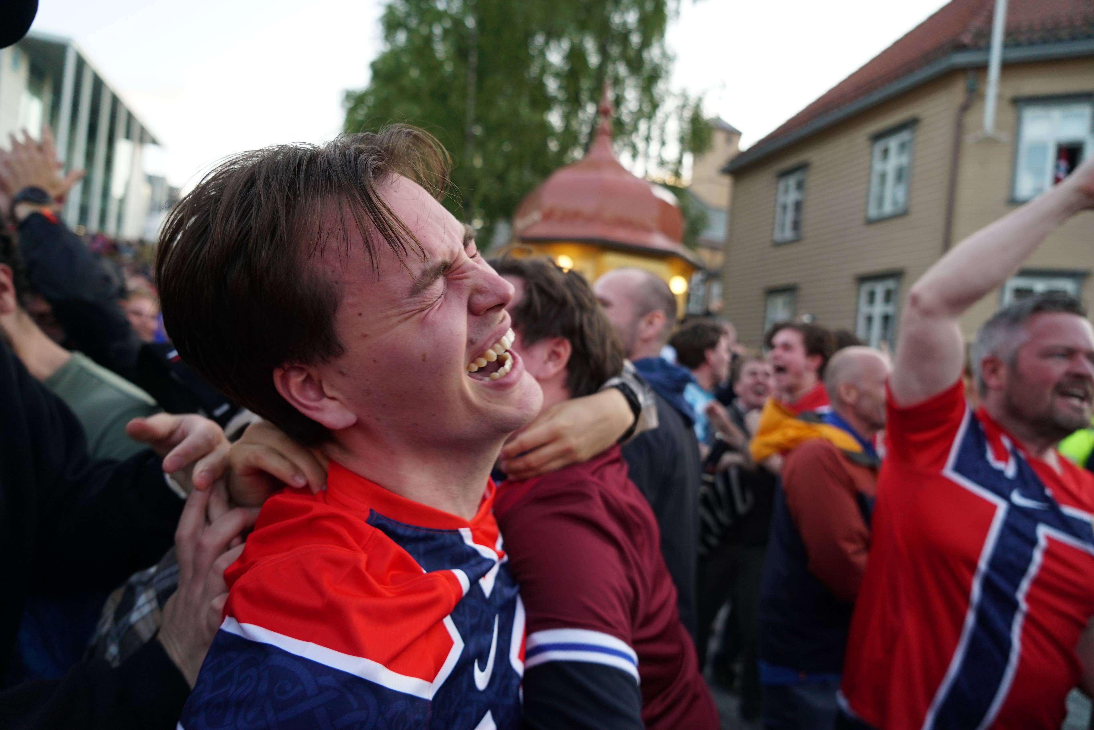 Folk i norske landslagsdrakter jubler i en folkemengde utendørs. (Bildebeskrivelsen er laget av en KI-tjeneste)