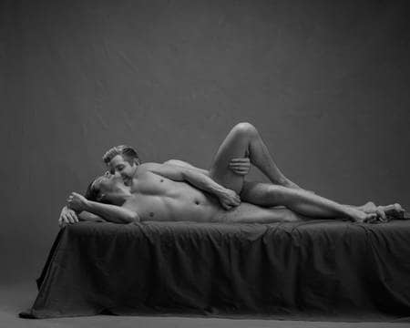 To nakne menn ligger inntil hverandre i skje på senga