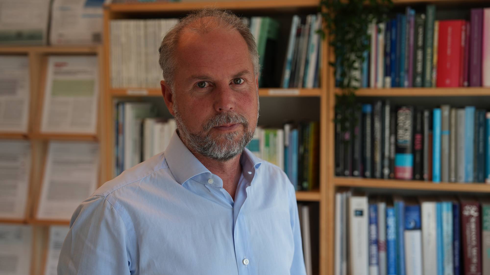 Thomas Clausen har på seg blå skjorte og poserer foran en vegg med bøker og publiserte forskningsartikler
