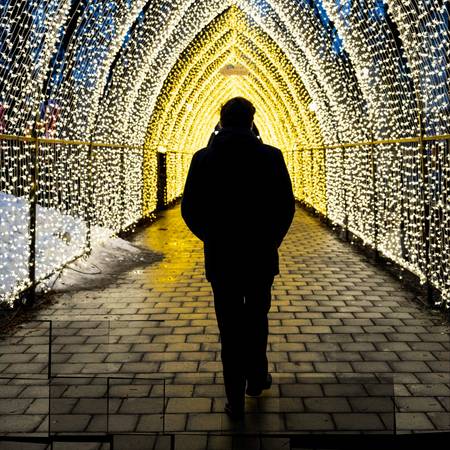 Silhuett av en mann som går gjennom en tunnel dekorert med julebelysning