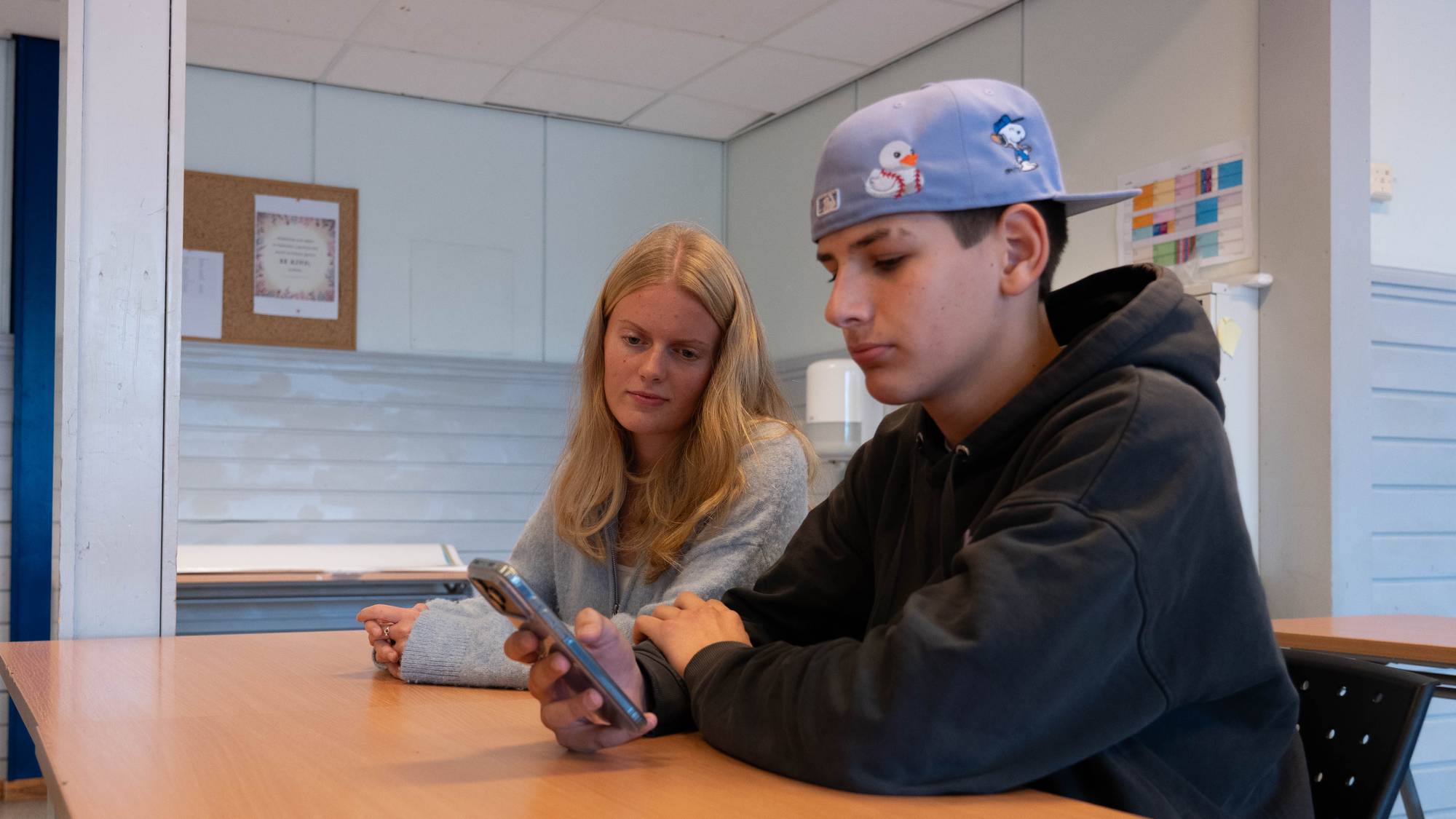 Annika og Phillip sitter sammen på klasserommet og ser i den ene mobilen