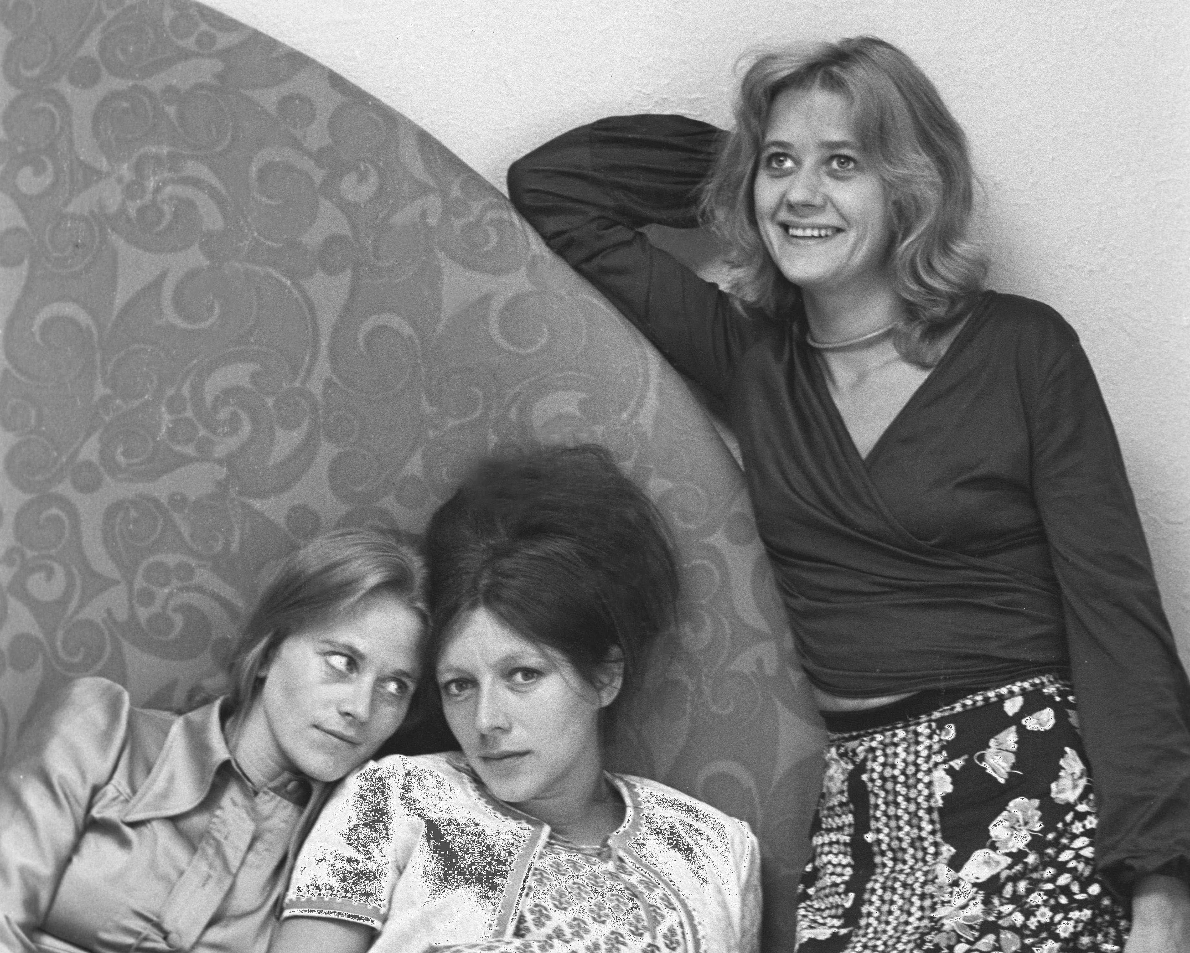 Tre damer sitter og lener seg på et stort møbel. Bildet er tatt i 1974 og damene har tidsriktige klær og hårfasonger.