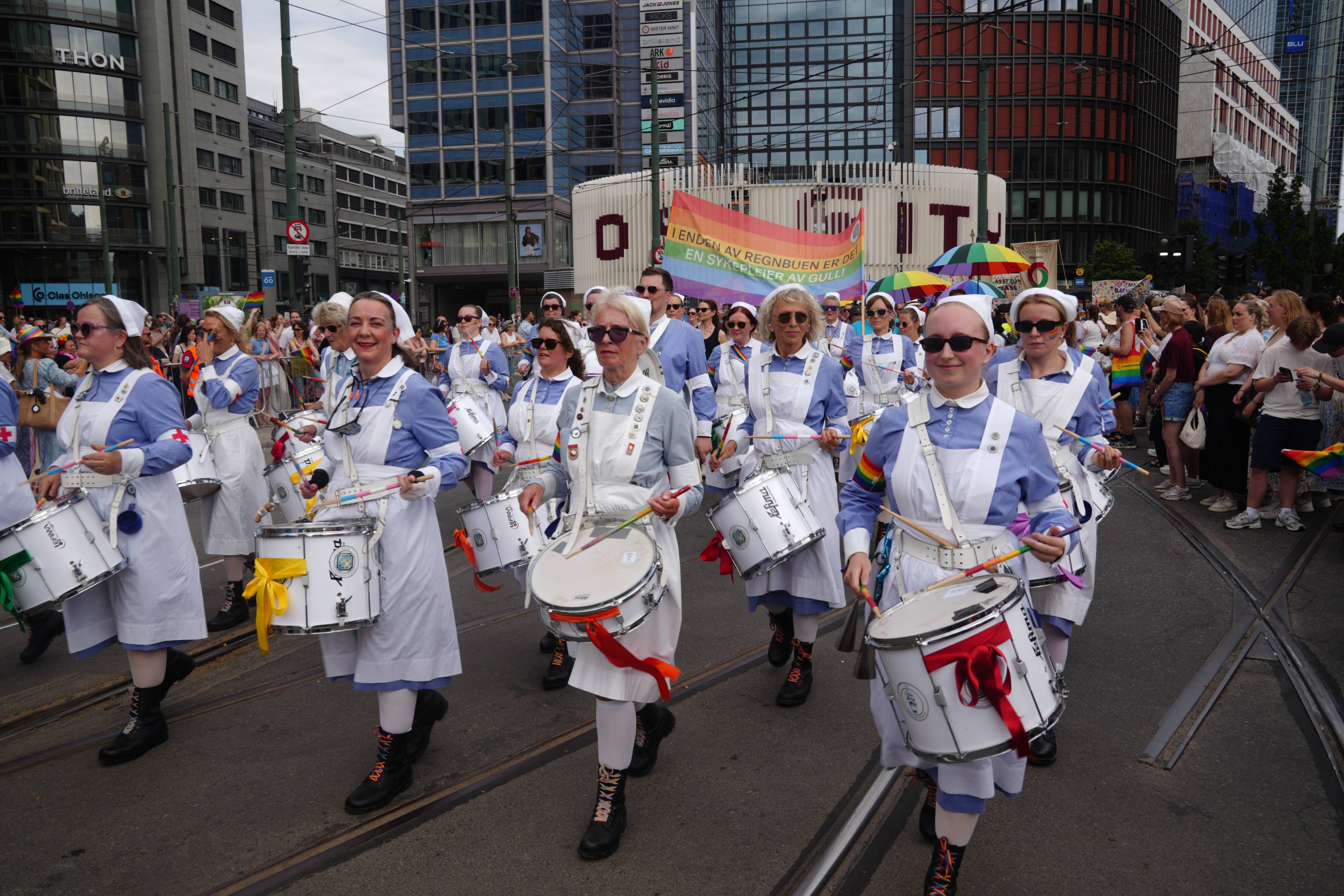 Sykepleiere i historiske uniformer spiller trommer i Pride-toget gjennom Oslo sentrum. (Bildebeskrivelsen er laget av en KI-tjeneste)