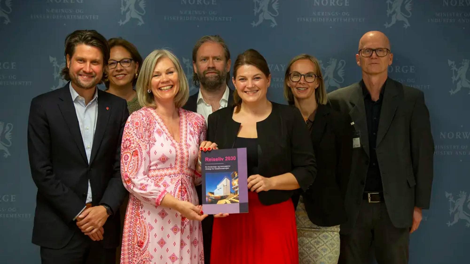 Regjeringsfoto med rapport i forgrunnen, som næringsministeren holder. 
