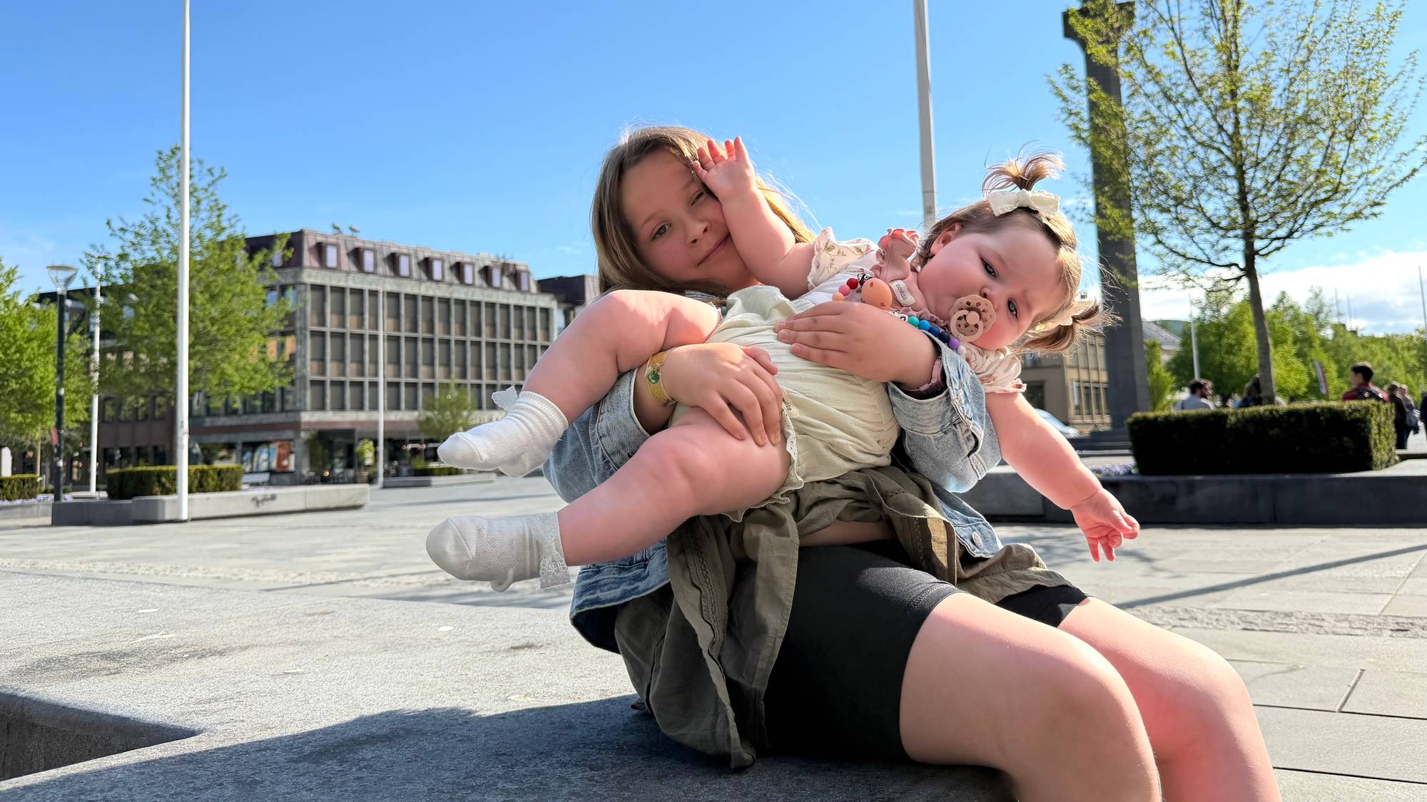 Norvella-Christin Dyrkorn Egge sitter på Torget i Trondheim med lillesøster Olava-Theoline på fanget. 