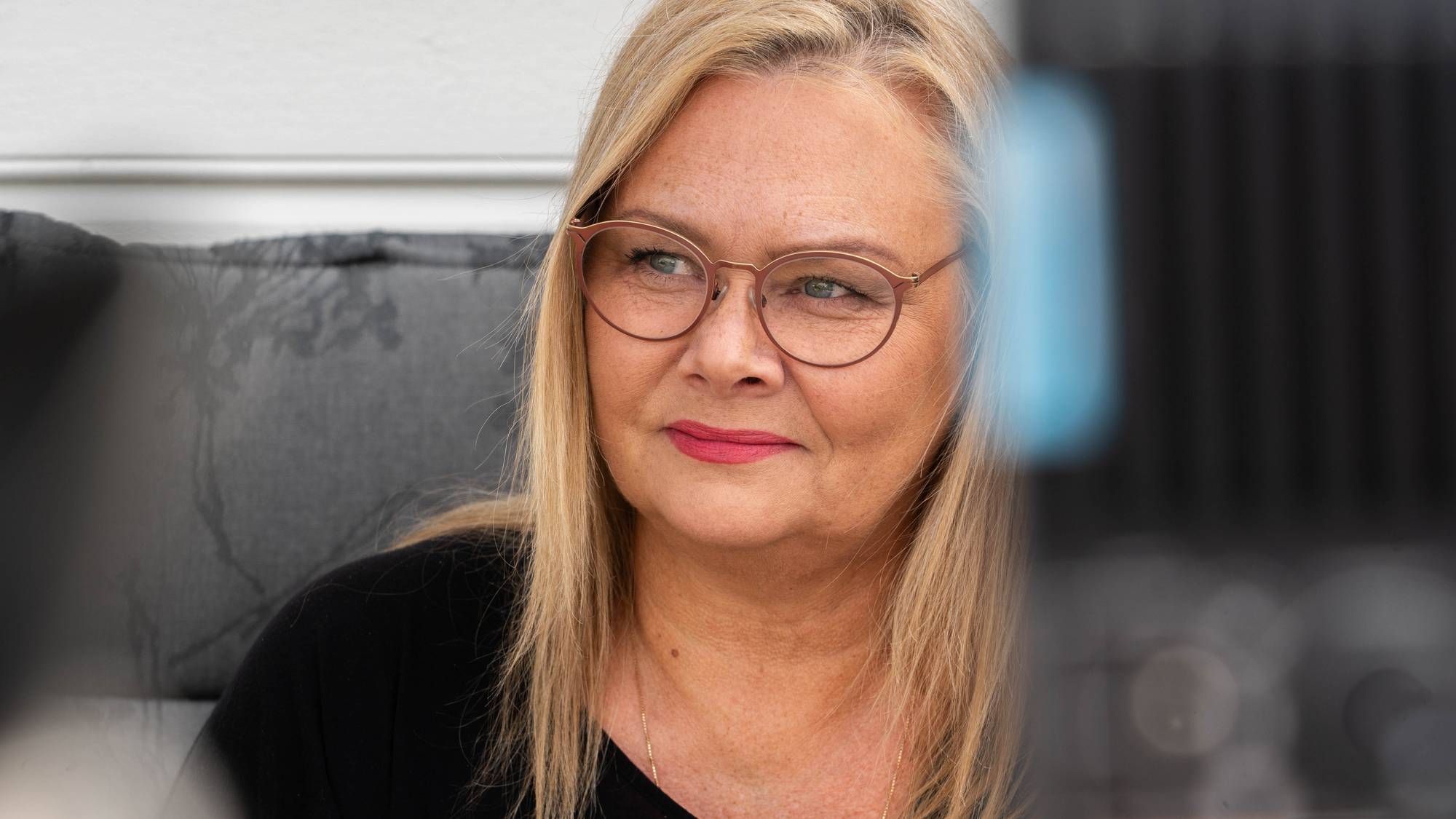 Portrett av ei kvinne med lyst hår, briller og mør topp.