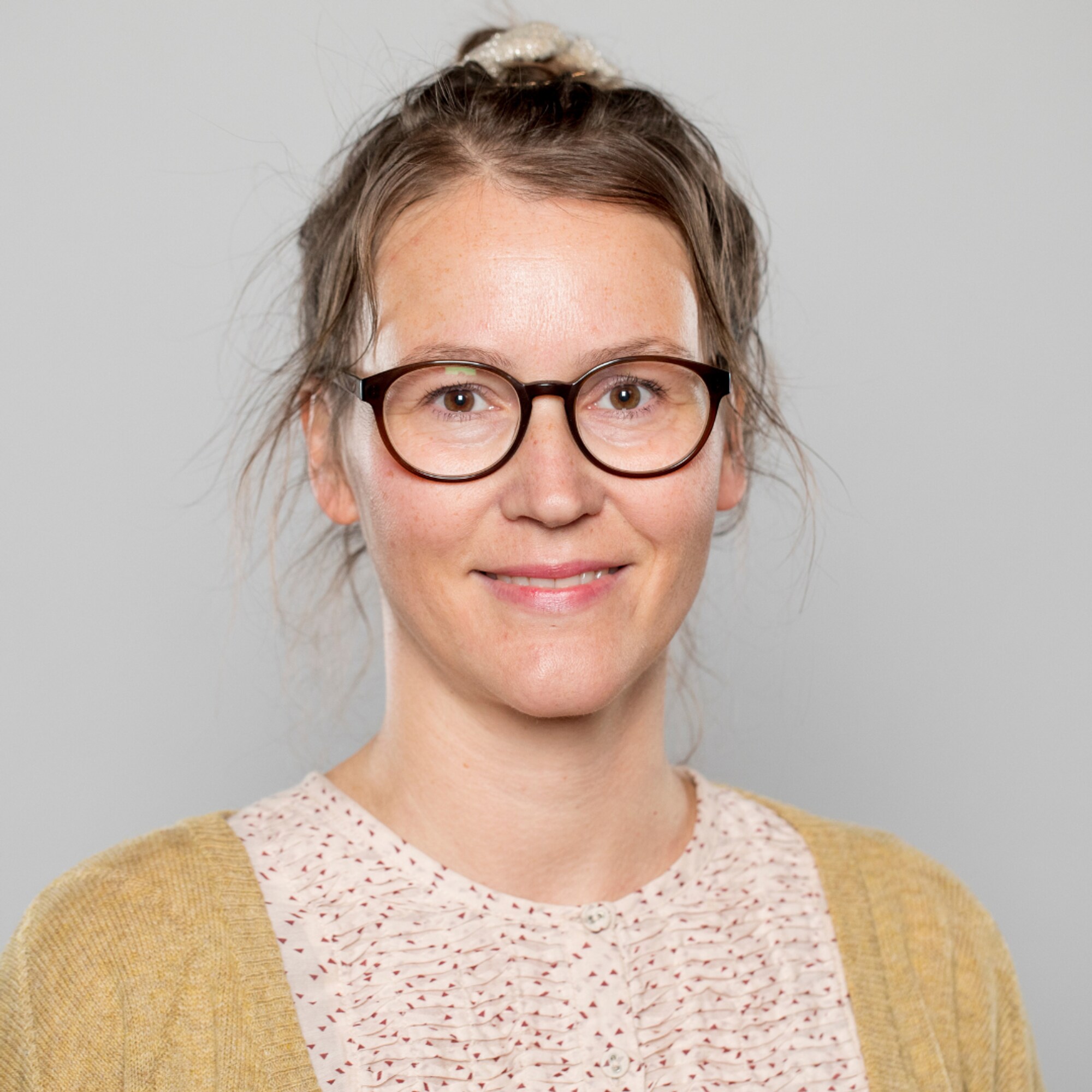 Kvinne med briller og oppsatt hår titter rett inn i kameraet.