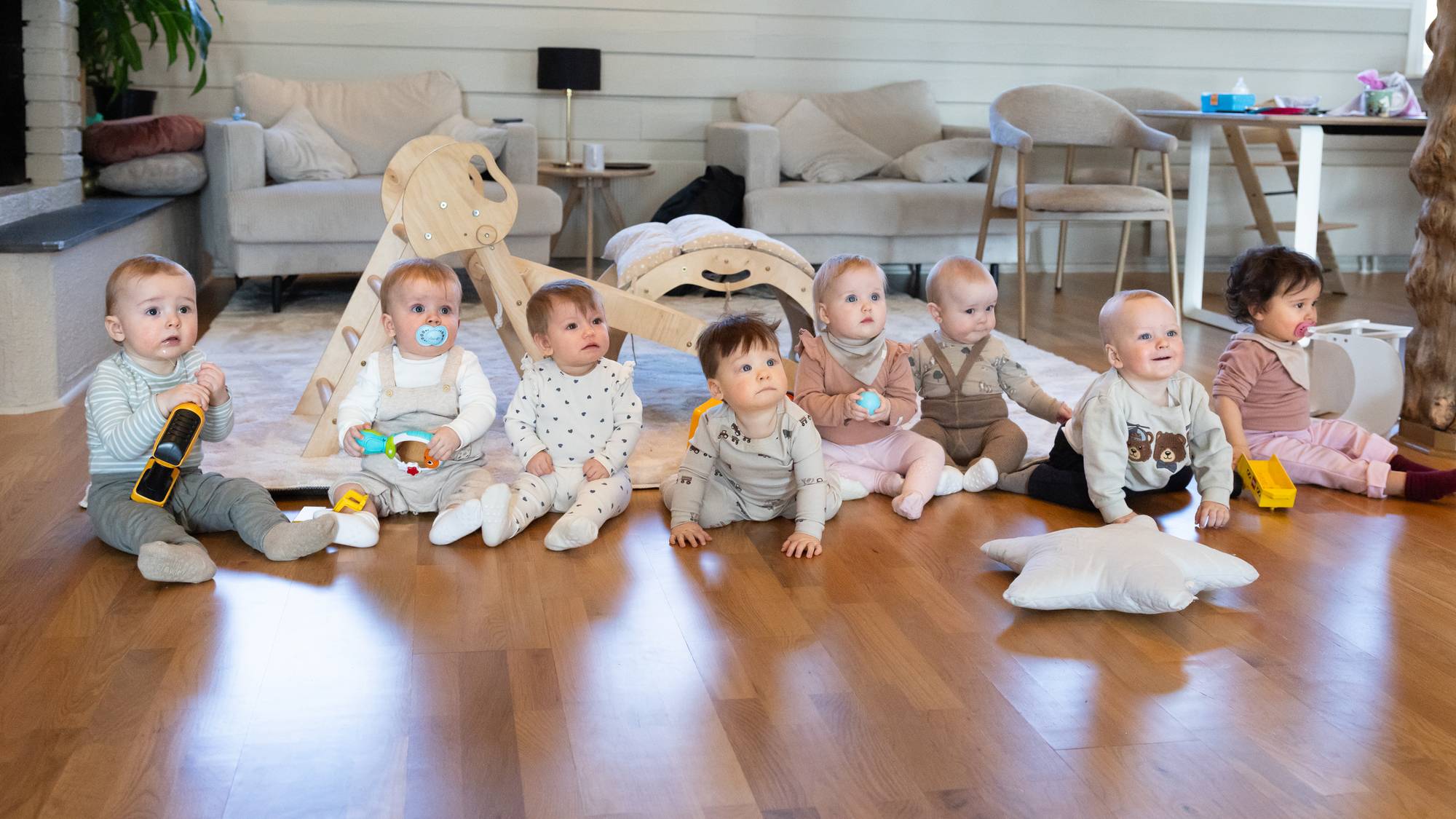 Gruppebilde av åtte babyer på gulvet i en stue
