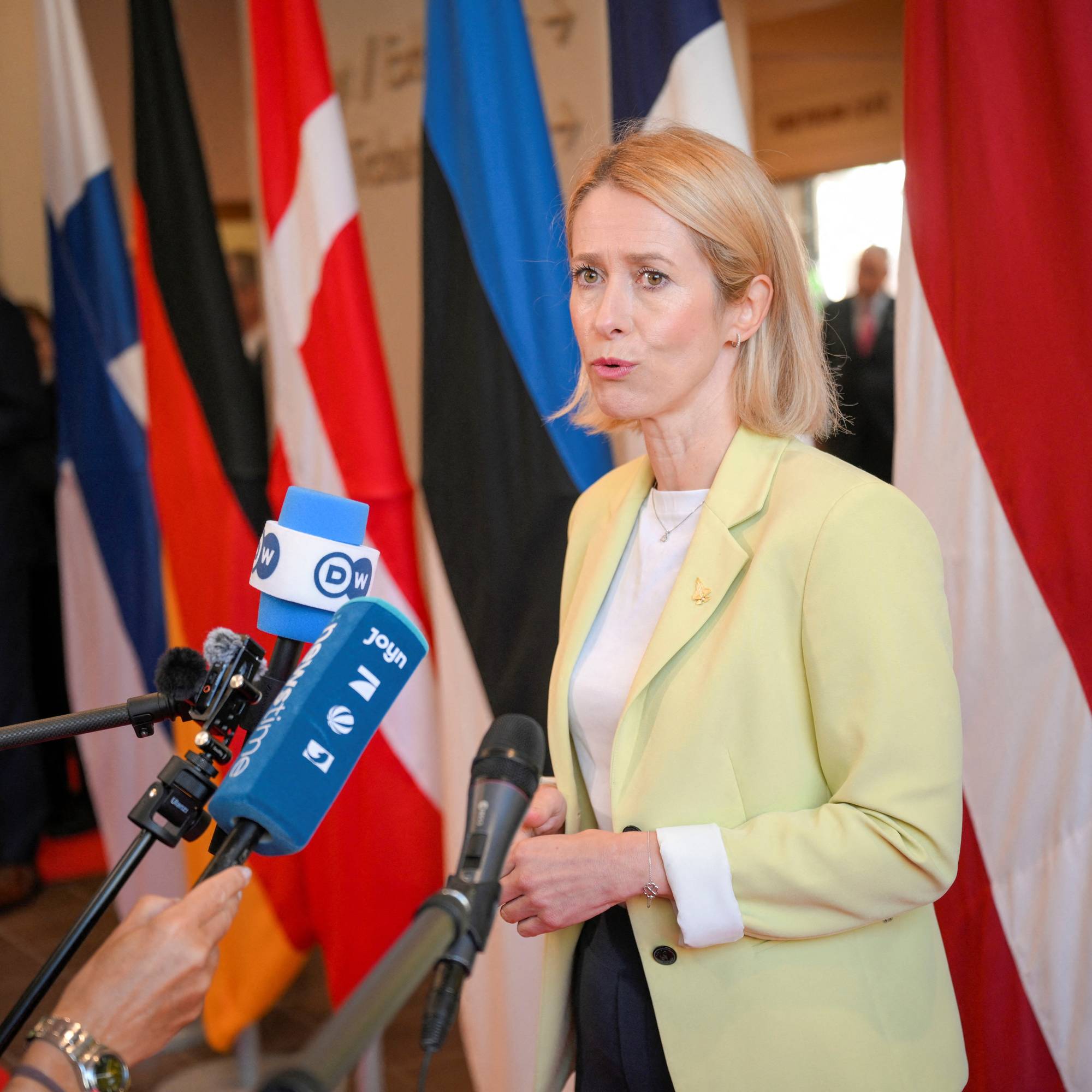 Kaja Kallas snakker til journalister foran flagg. (Bildebeskrivelsen er laget av en KI-tjeneste)
