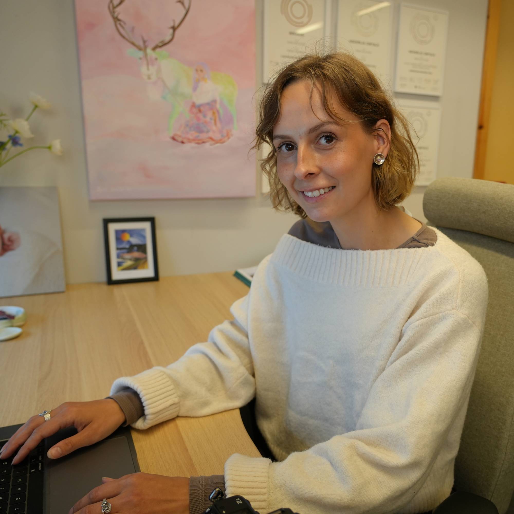 Kvinne med lys genser sitter ved et skrivebord med en bærbar datamaskin. (Bildebeskrivelsen er laget av en KI-tjeneste)