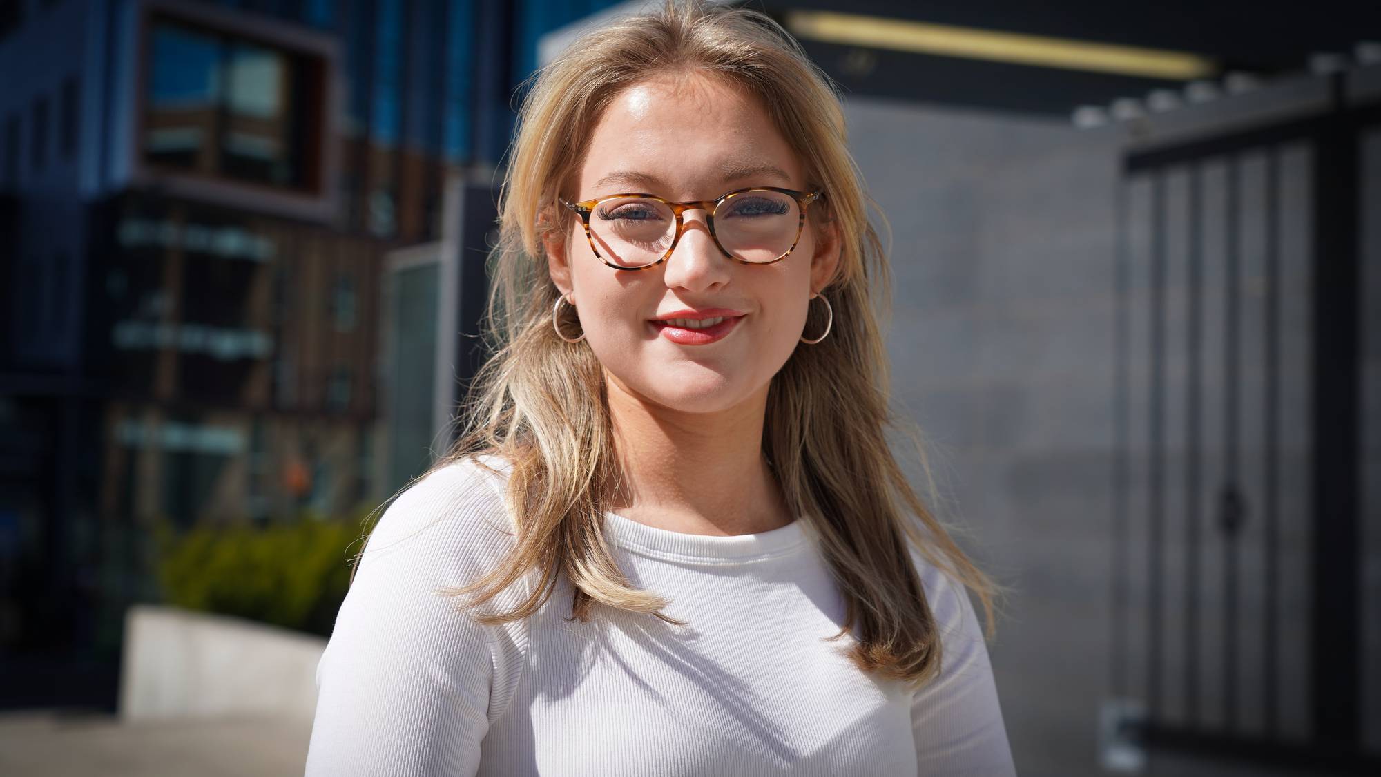 En ung blond kvinne med briller smiler til kameraet
