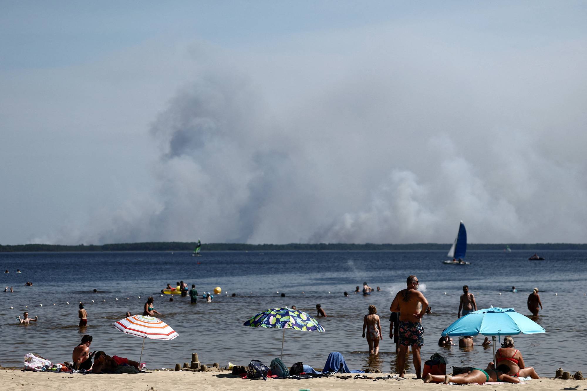 Folk på strand med røyk fra branner i distansen
