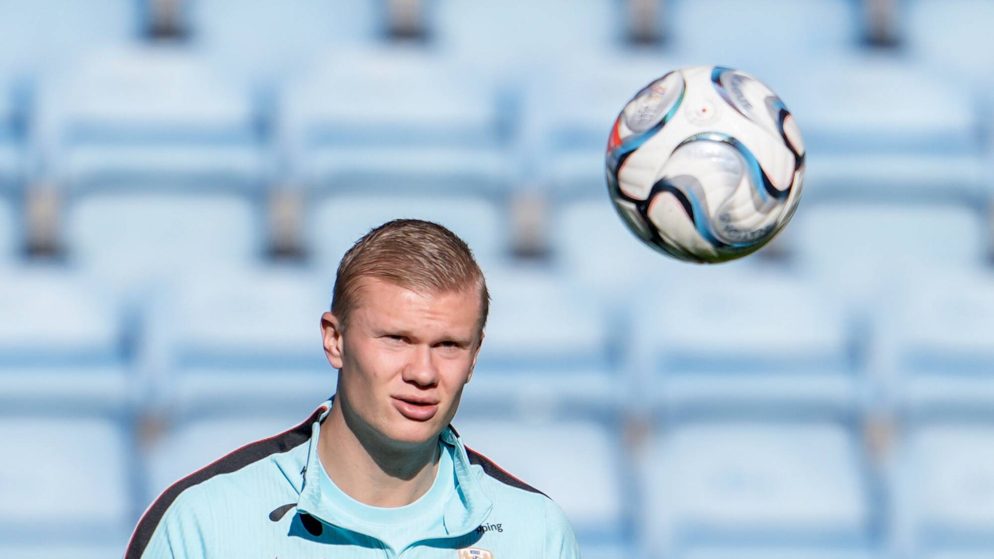 Erling Braut Haaland under fotballtrening med en ball foran seg og tomme tribuner i bakgrunnen. (Bildebeskrivelsen er laget av en KI-tjeneste)