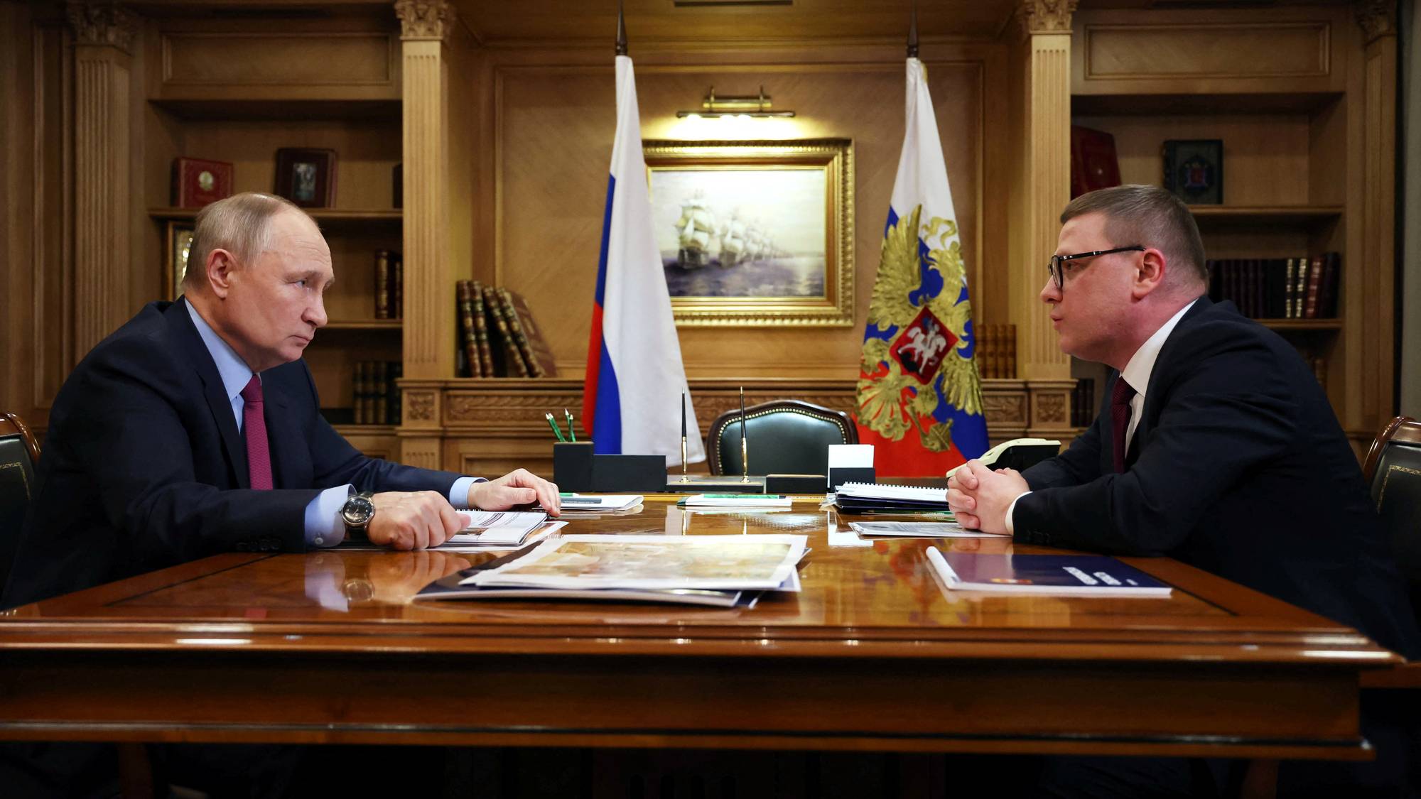 Russlands president Vladimir Putin og utenriksminister Sergej Lavrov møtes ved et polert trebord. Begge mennene er kledd i dress og sitter overfor hverandre. Bak dem henger russiske flagg og et maleri av et seilskip. (Bildebeskrivelsen er laget av en KI-tjeneste)