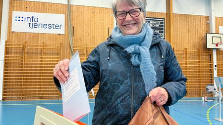 En smilende kvinne slipper stemmeseddelen ned i en stemmeurne