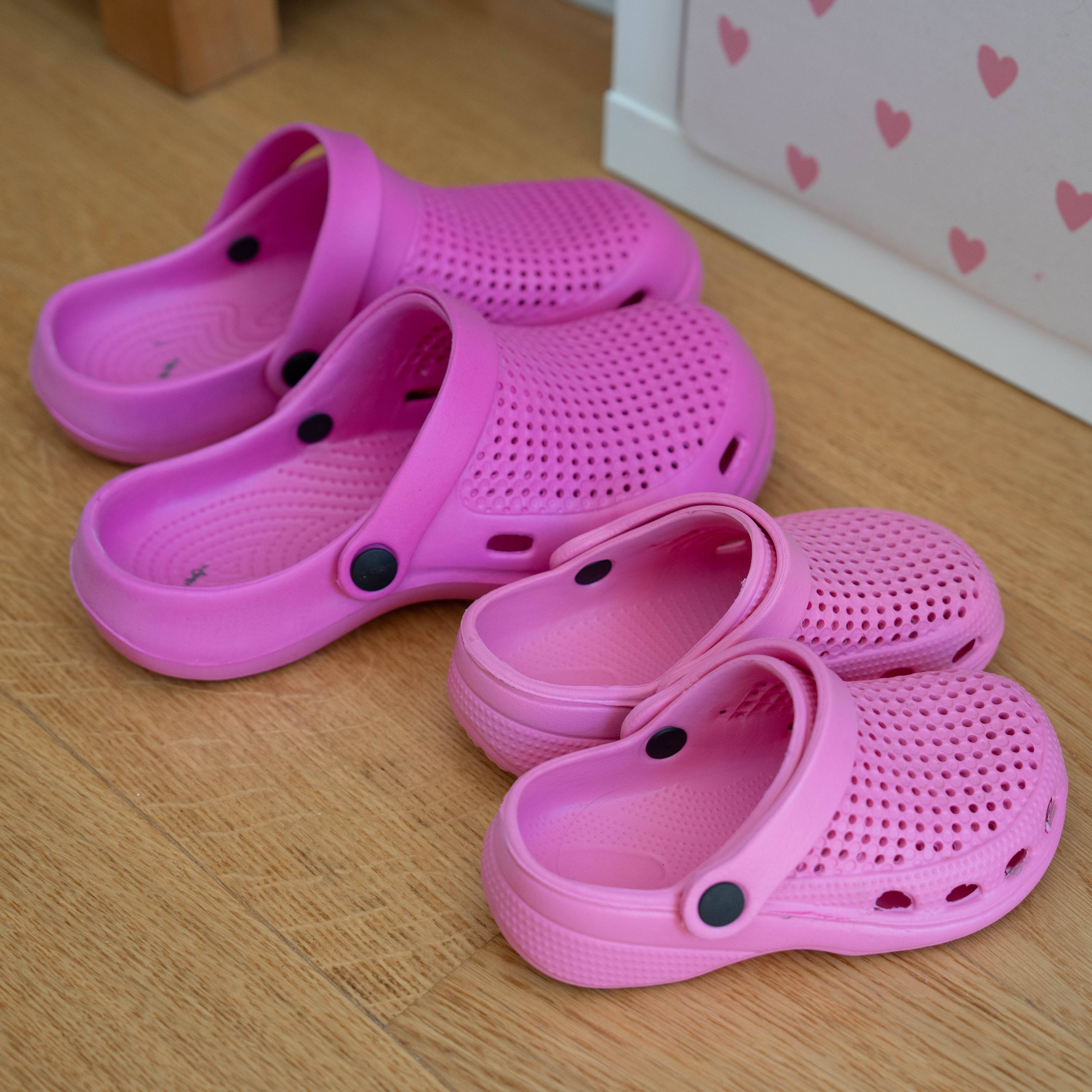 Biletet viser to par med rosa crocs som står ved sida av kvarandre på golvet. Det eine paret er i vaksenstorleik, og det er andre er i barnestorleik.