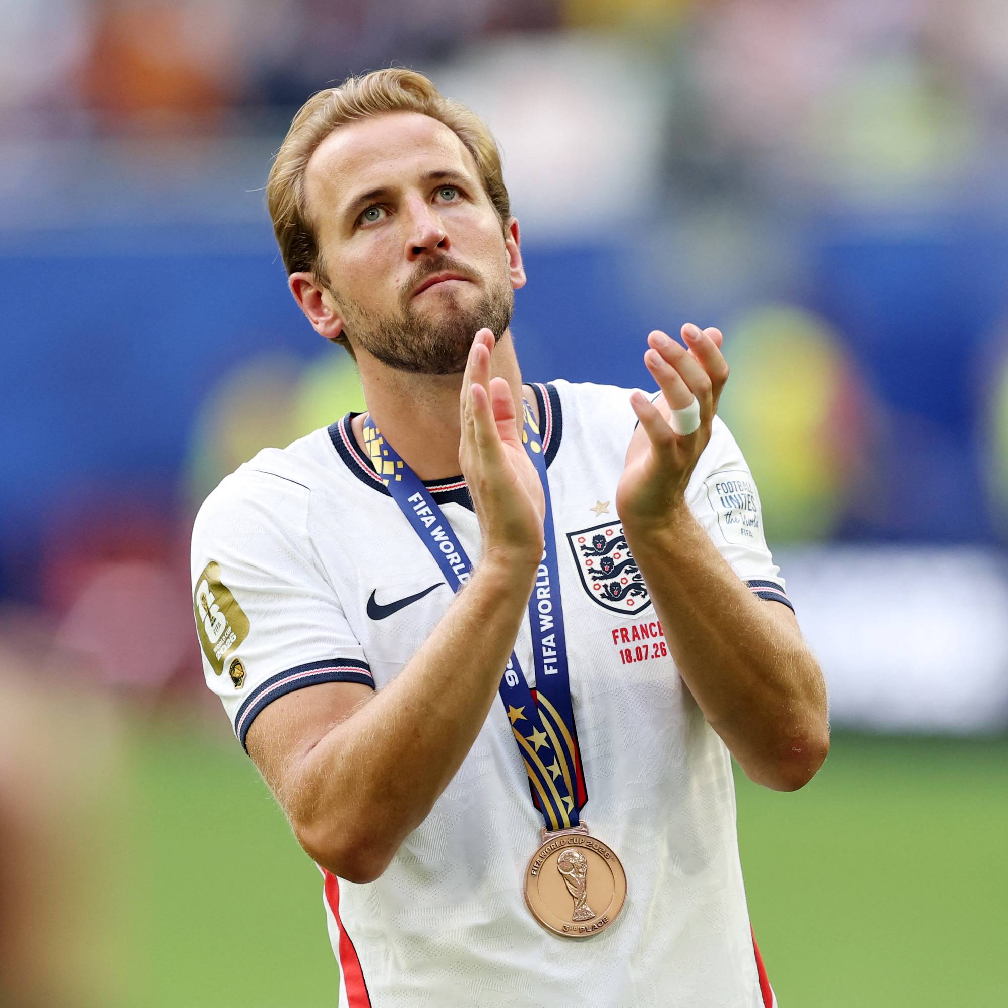 En mann med hvit fotballdrakt og medalje rundt halsen klapper