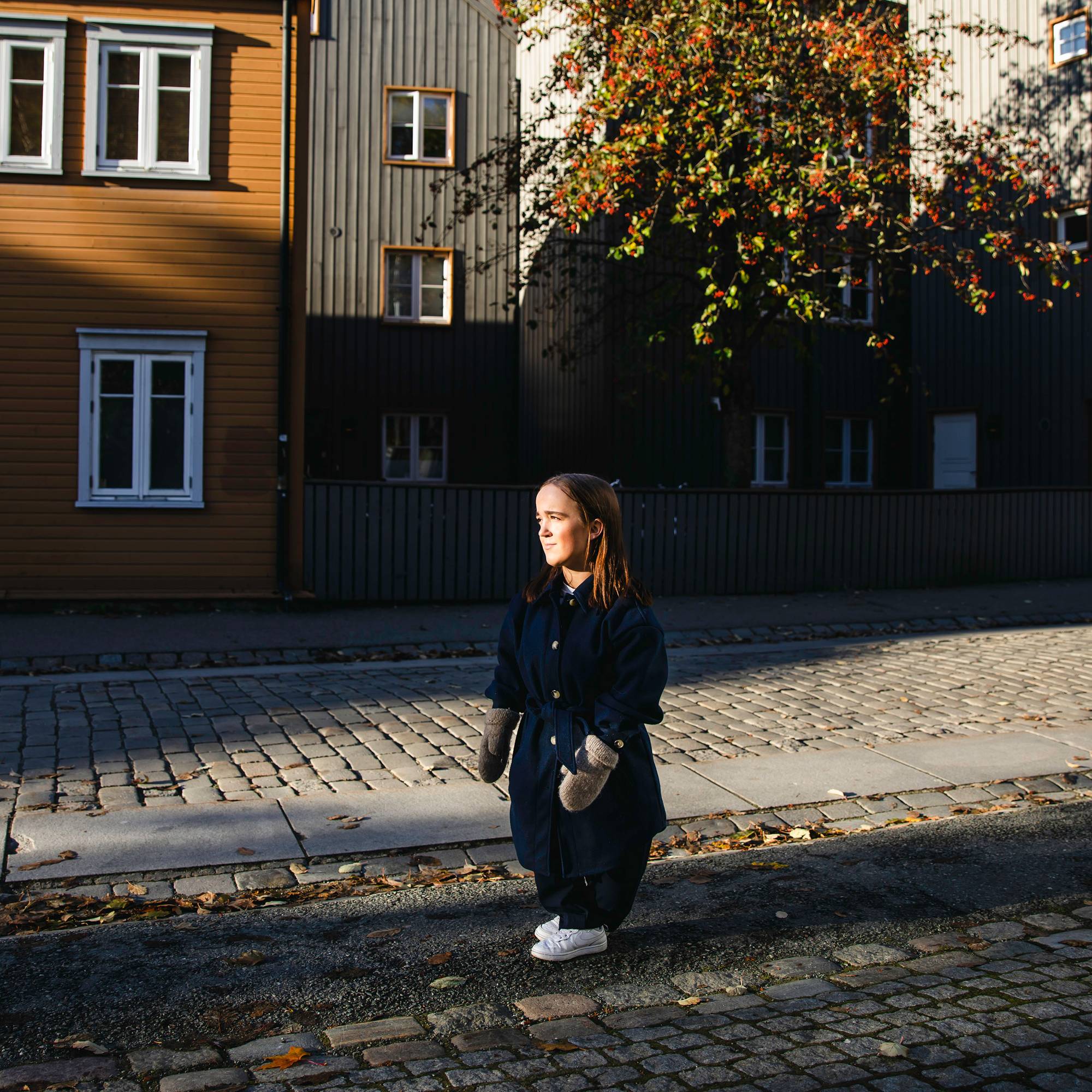 Oda har på seg en vinterjakke og votter. Hun står på brosteinen ved Bakklandet og ser til siden. Hun har et mykt og nøytralt blikk. 