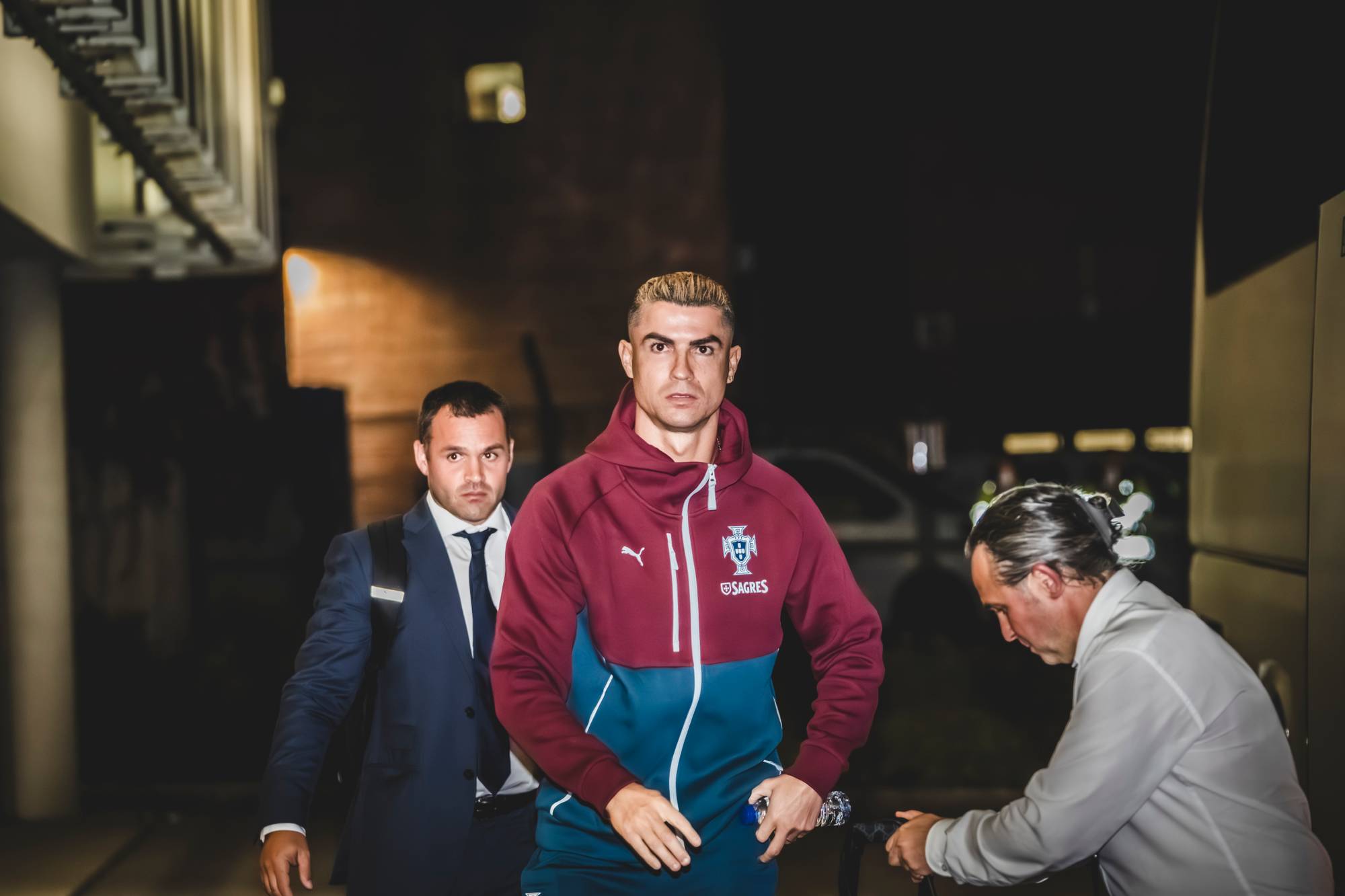 Cristiano Ronaldo går utendørs kledd i Portugals landslagstøy, flankert av to menn i dress.