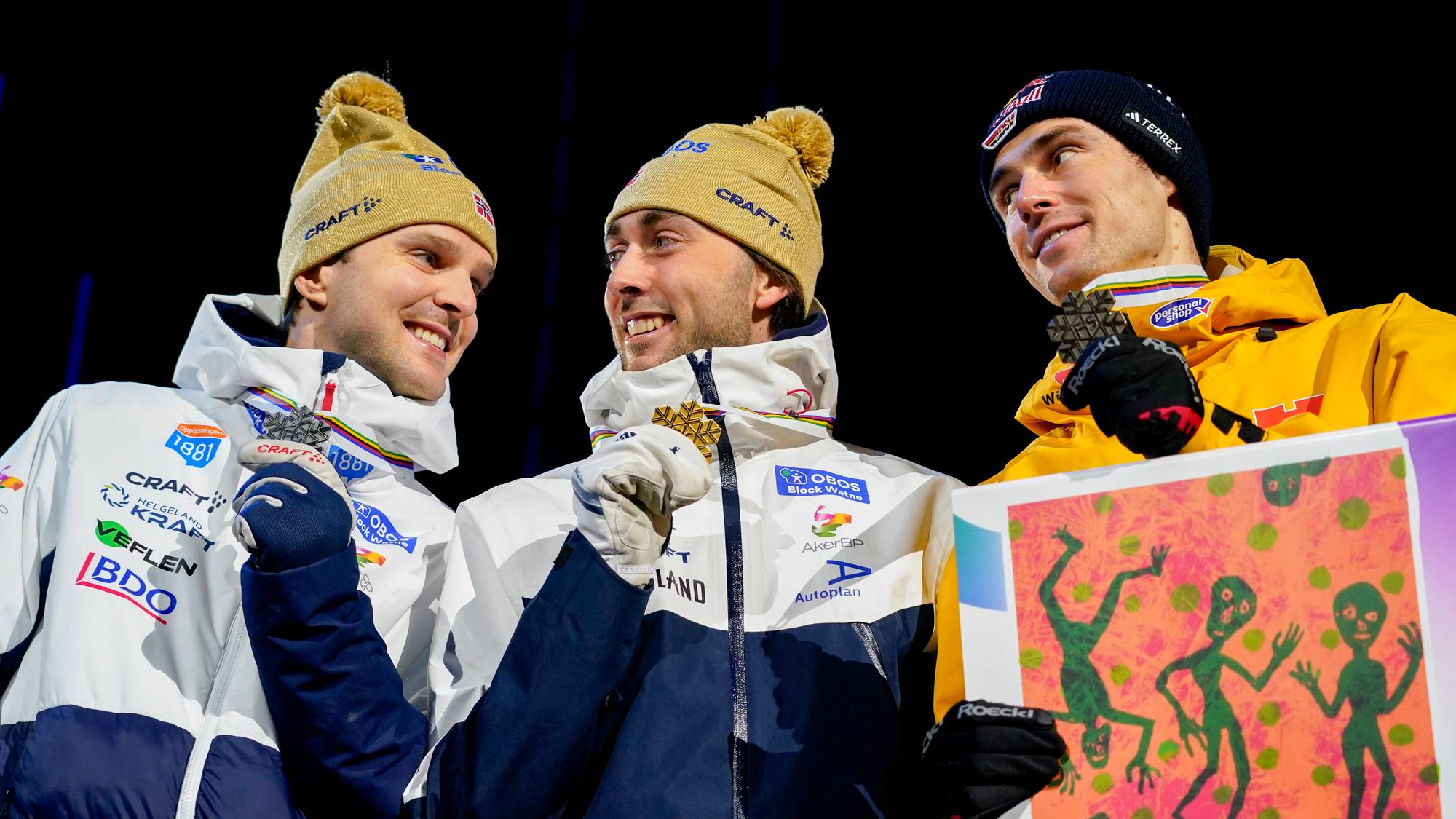 Tre langrennsløpere med medaljer rundt halsen under en premieseremoni på kveldstid. (Bildebeskrivelsen er laget av en KI-tjeneste)