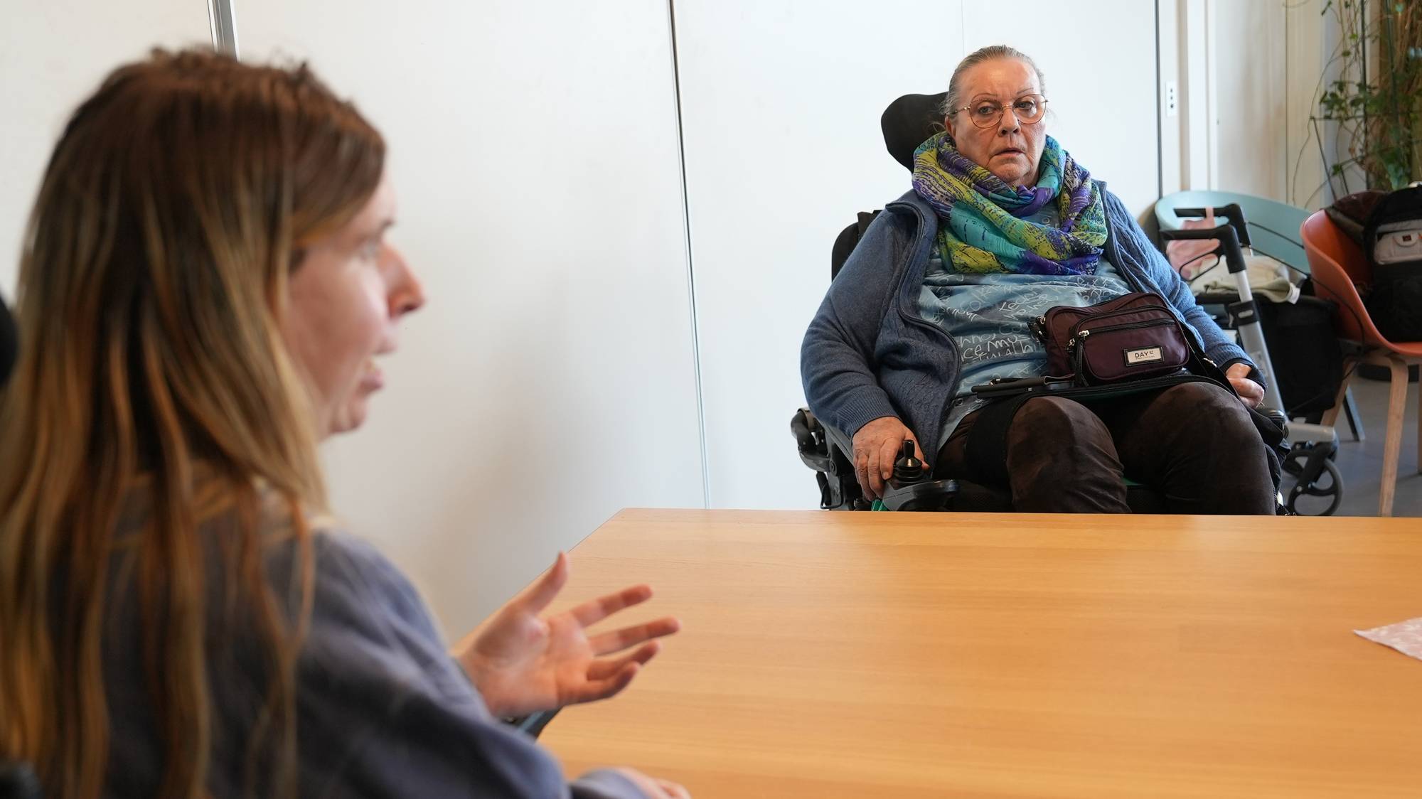 Rina Wesenberg og Anne Karin Eriksen, to kvinner sitter i rullestolene sine på hver sin side av et et bord.