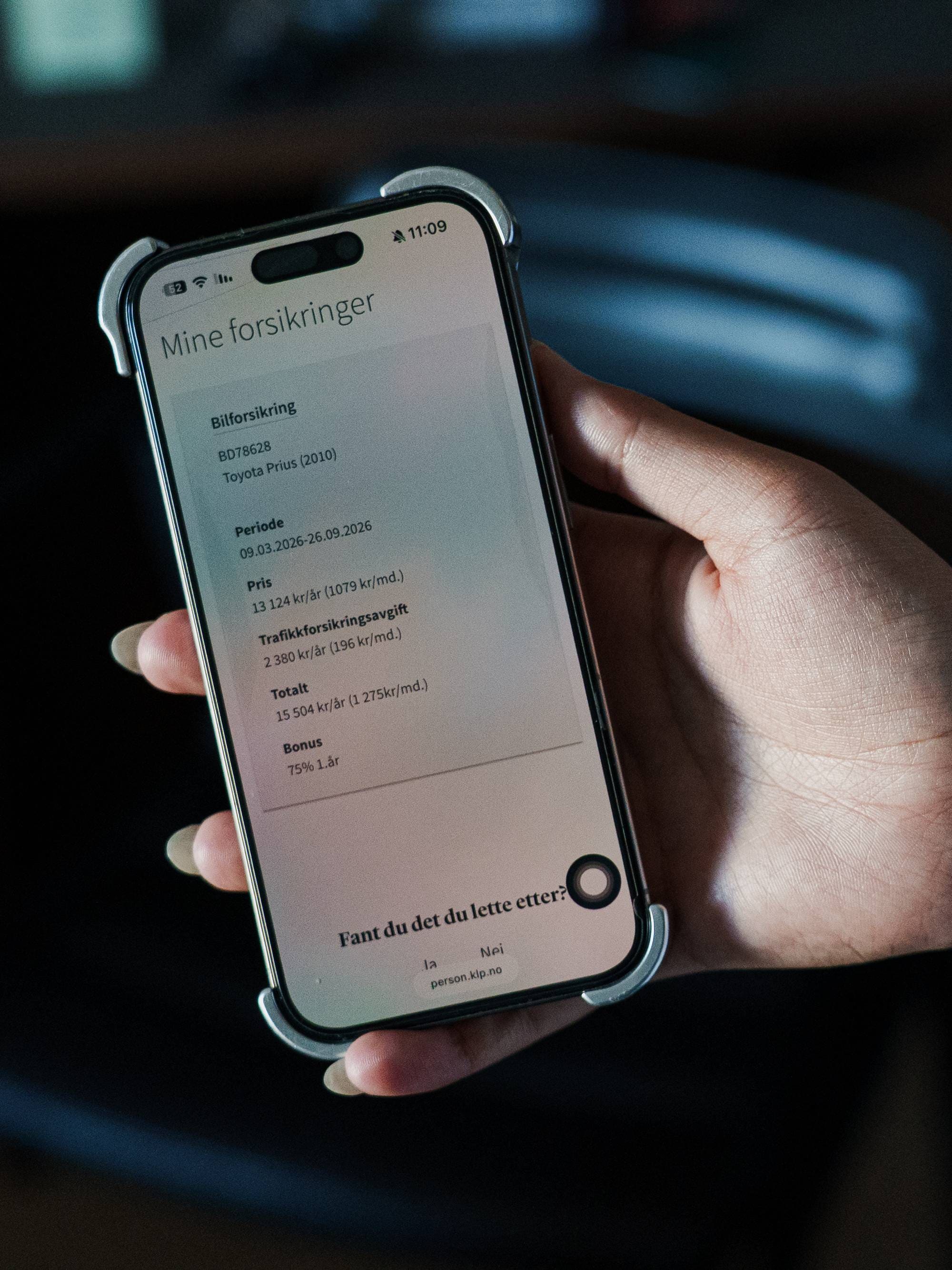 Person holder en mobiltelefon som viser forsikringsopplysninger på skjermen. (Bildebeskrivelsen er laget av en KI-tjeneste)