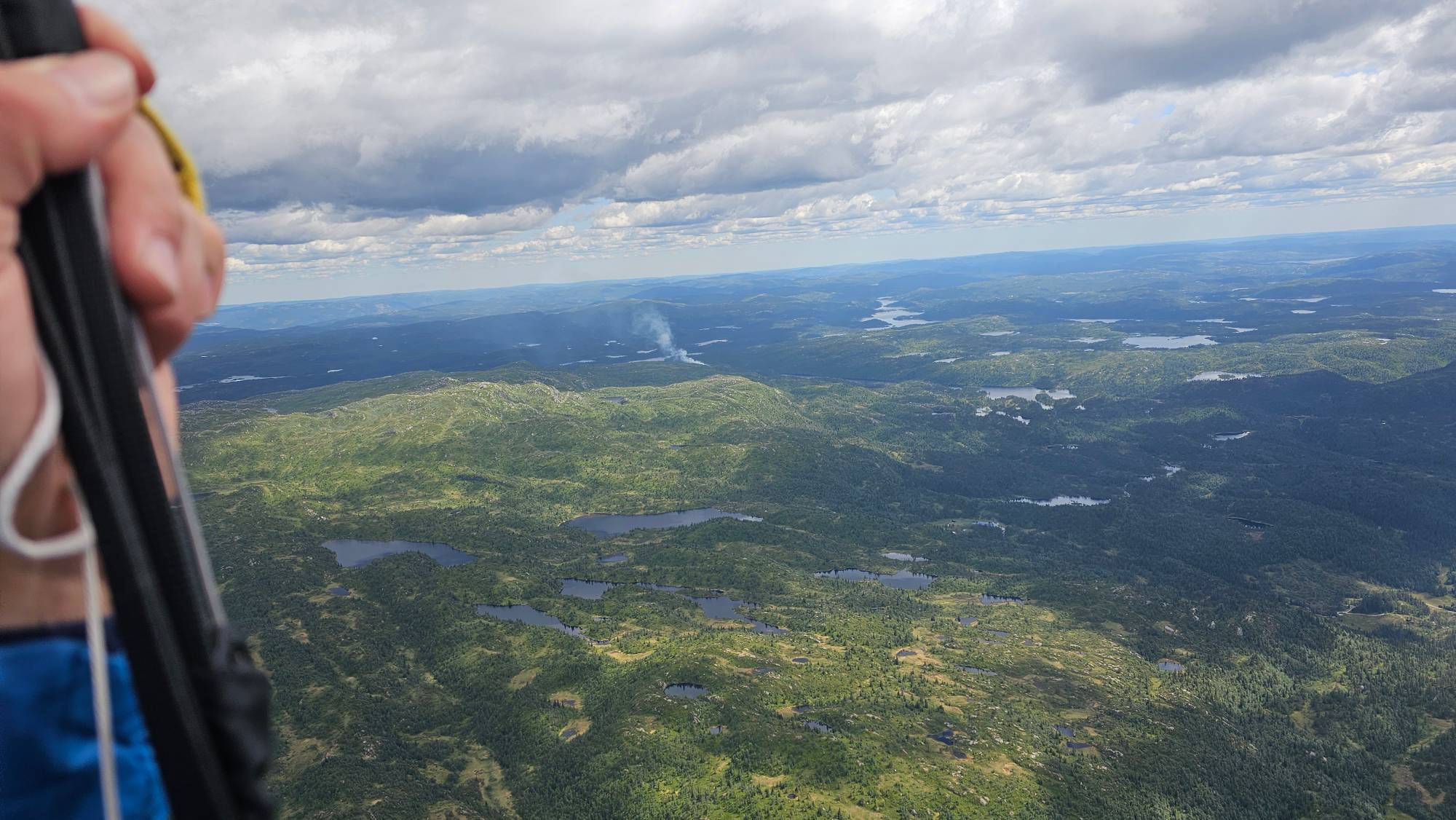 Luftfoto over skog og vann med en tydelig røyksøyle fra en skogbrann i det fjerne. (Bildebeskrivelsen er laget av en KI-tjeneste)