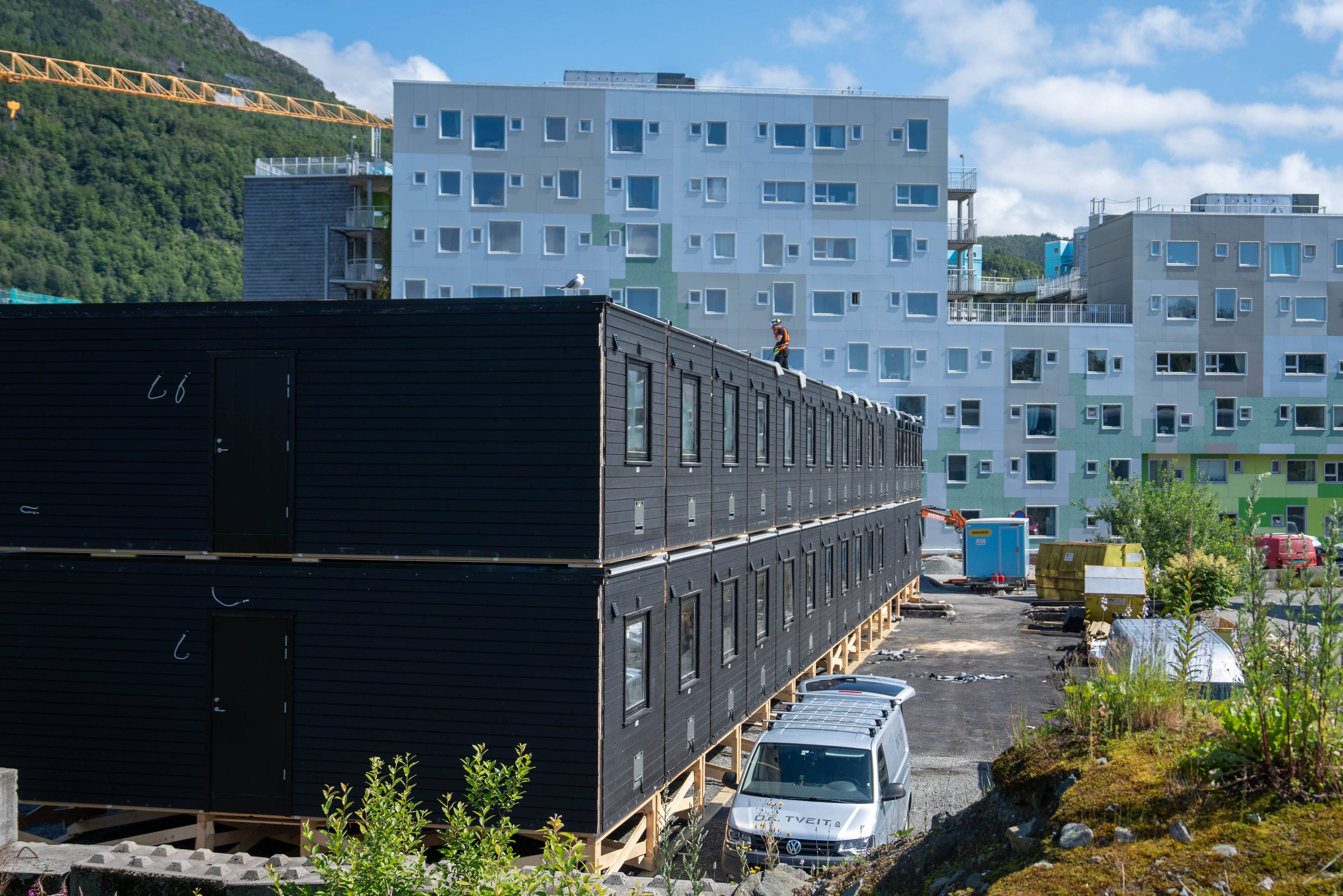 Svart brakkerigg i to etasjar ved ein byggjeplass med leileghetsbygg i bakgrunnen.