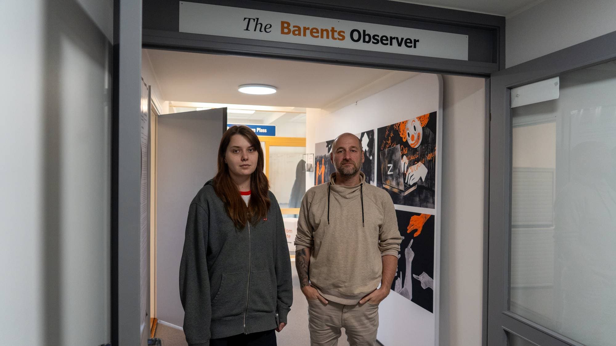 Kvinne og mann står i inngangen til kontorlokalene til The Barents Observer. (Bildebeskrivelsen er laget av en KI-tjeneste)