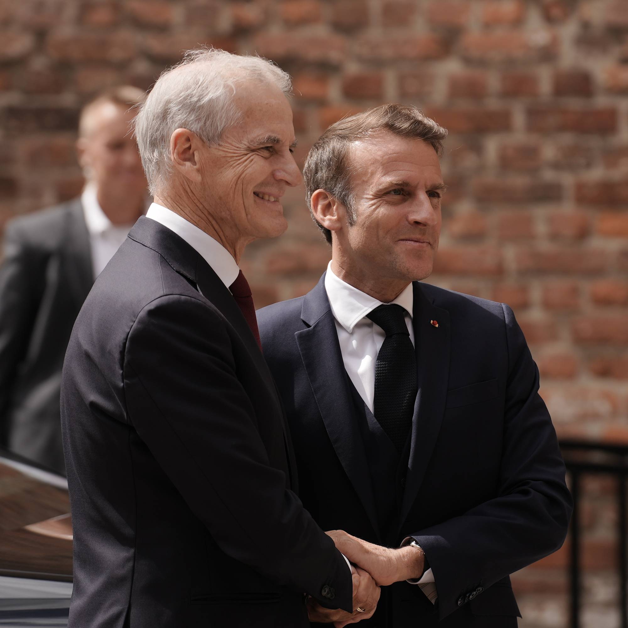 Jonas Gahr Støre smiler mens han håndhilser på Frankrikes president Emmanuel Macron