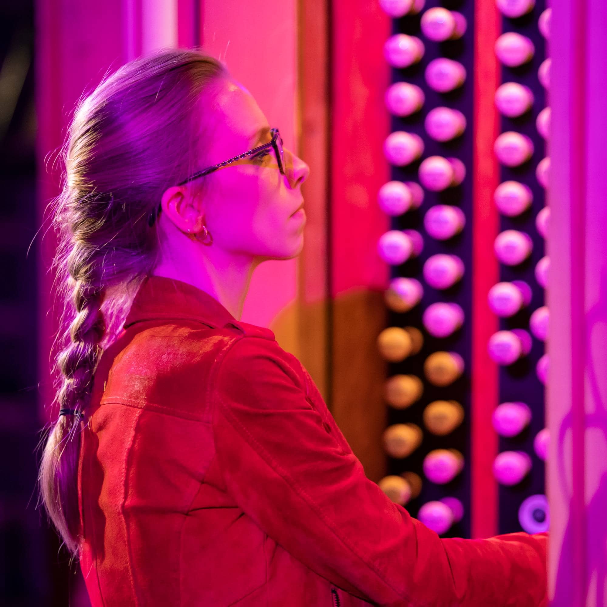 Anna Lapwood spiller orgel. Hun har på seg en rød jakke og spillepulten er badet i rosa lys.