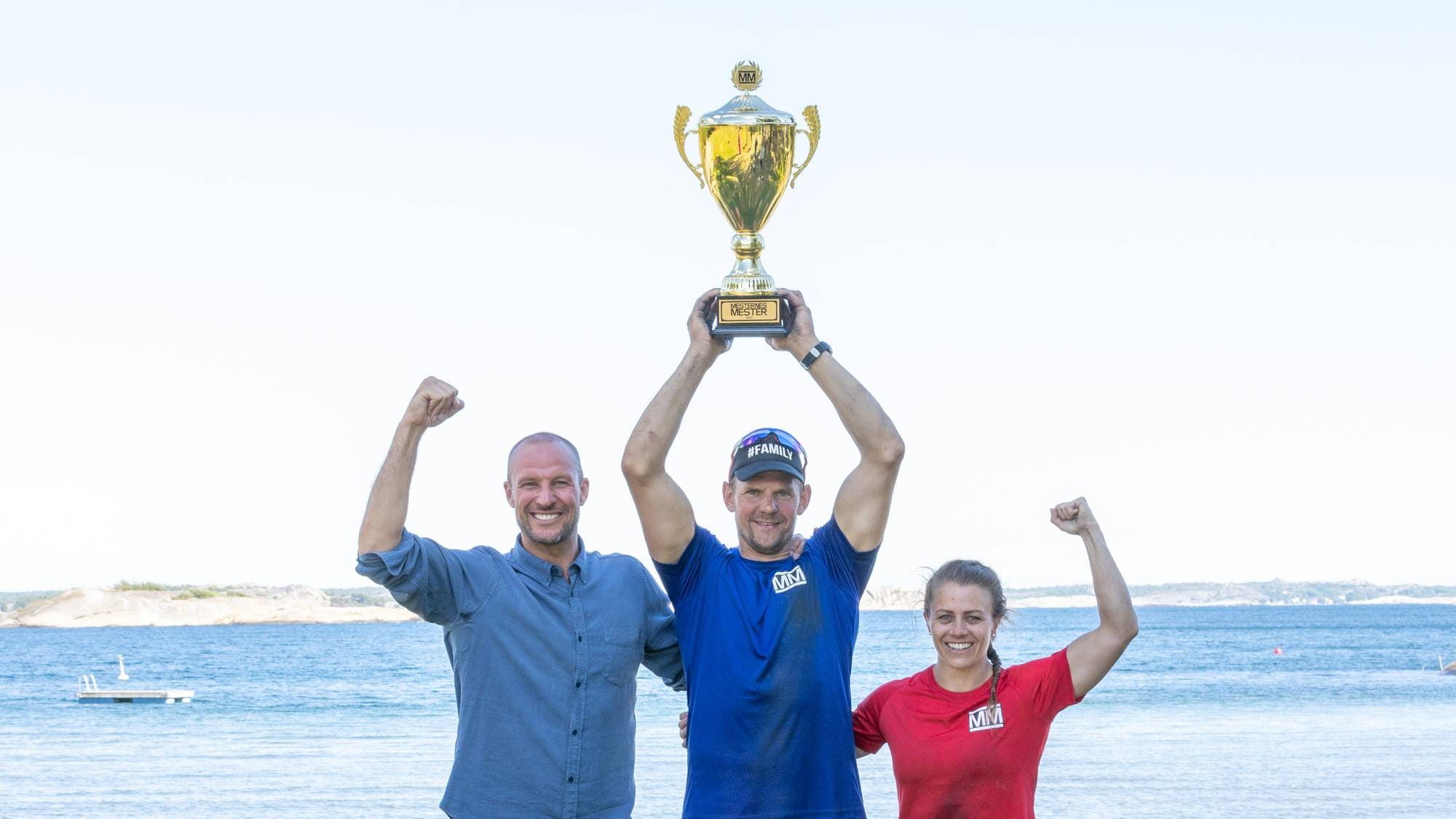 Vinner av Mesternes mester Olaf Tufte hever pokalen over hodet på stranda i Sandefjord, står mellom finalist Kristin Holte og programleder Aksel Lund Svindal