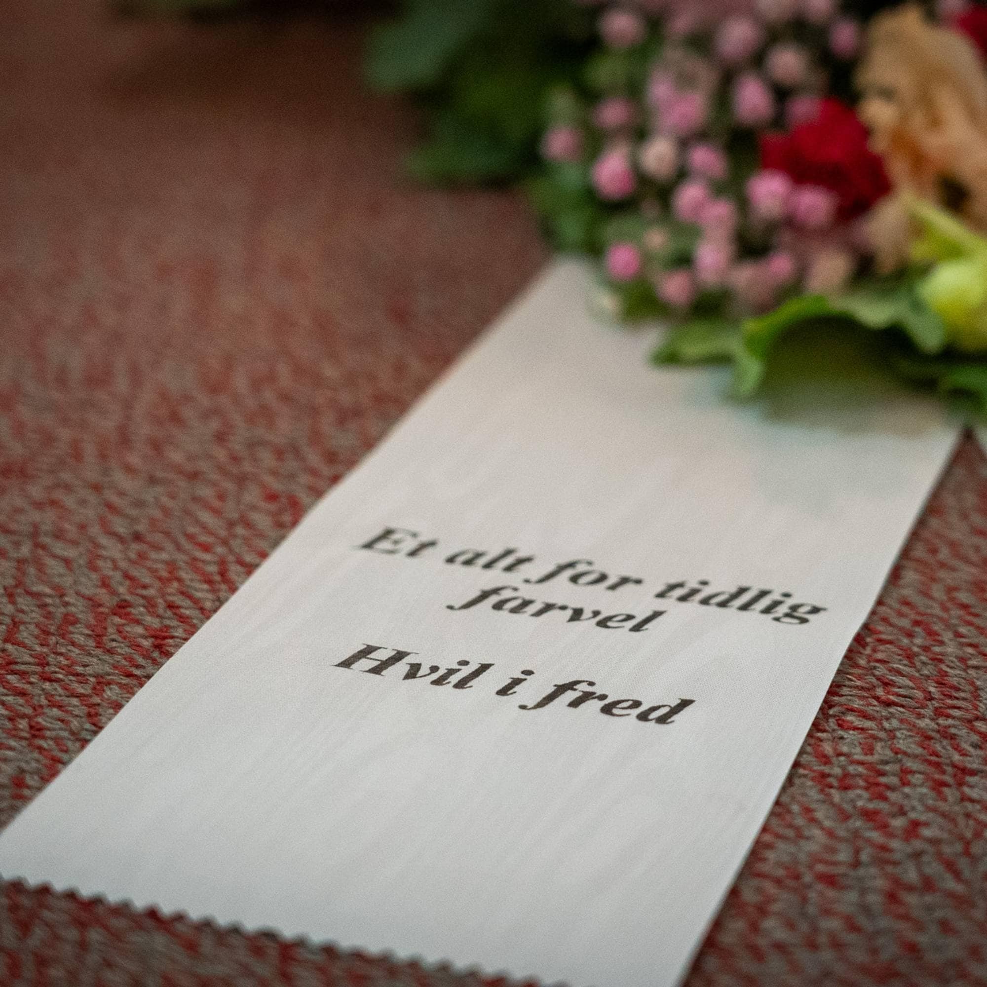 En blomsterkrans med teksten "Et alt for tidlig farvel. Hvil i fred"