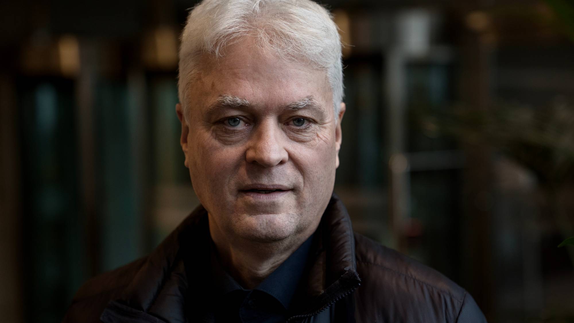 Mann med hvitt hår og nøytralt ansiktsuttrykk ikledd svart boblejakke