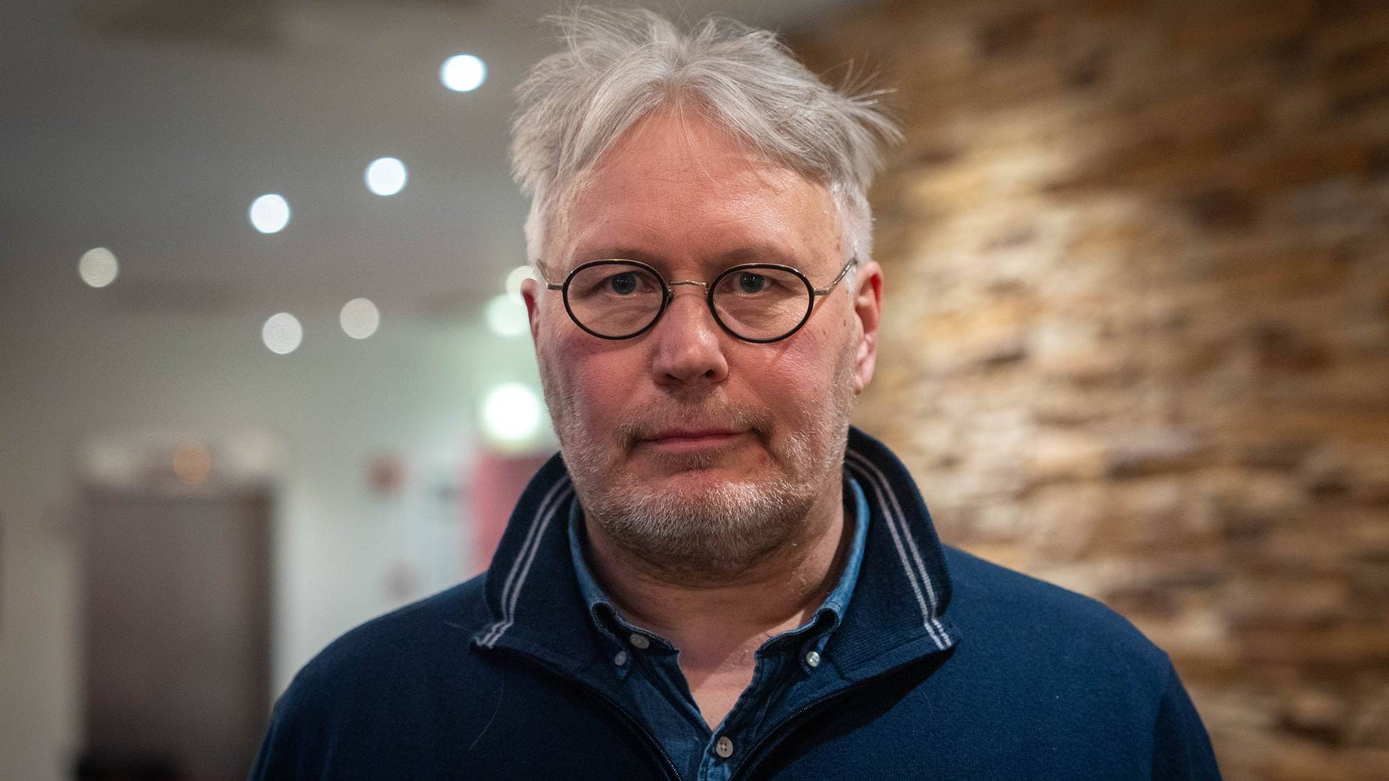 Skjalg Fjellheim står fremfor en murvegg og heisen på Scandic i Alta.