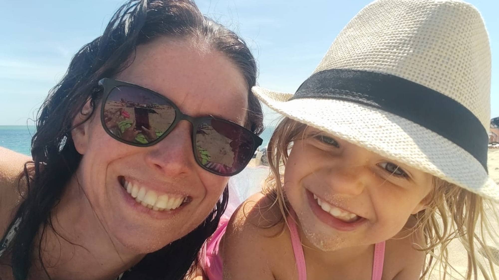 En kvinne og et barn smiler på stranden