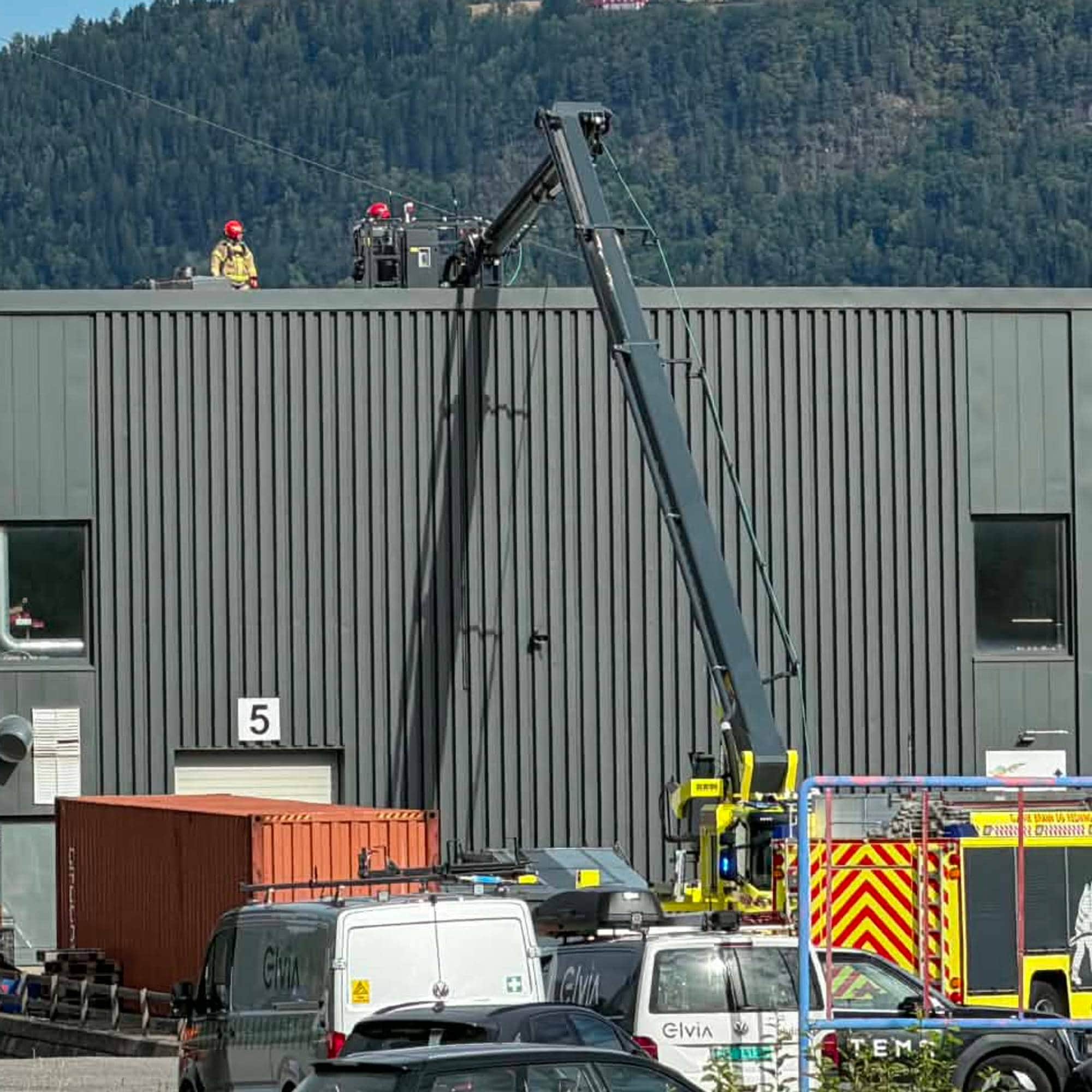 Brannvesenet arbeider på taket av en industribygning ved Biri næringspark med en lift. (Bildebeskrivelsen er laget av en KI-tjeneste)
