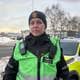 Sunniva Skurtveit / NRK En polititjenestemann i uniform står foran en politibil i snødekte omgivelser. Tjenestemannen bærer to radiosendere på brystet og har på seg en lue med politiemblem. I bakgrunnen er det flere biler og trær, med et skyet himmel som gir en dempet atmosfære. Dette bildet kan indikere en pågående politioperasjon eller overvåking.