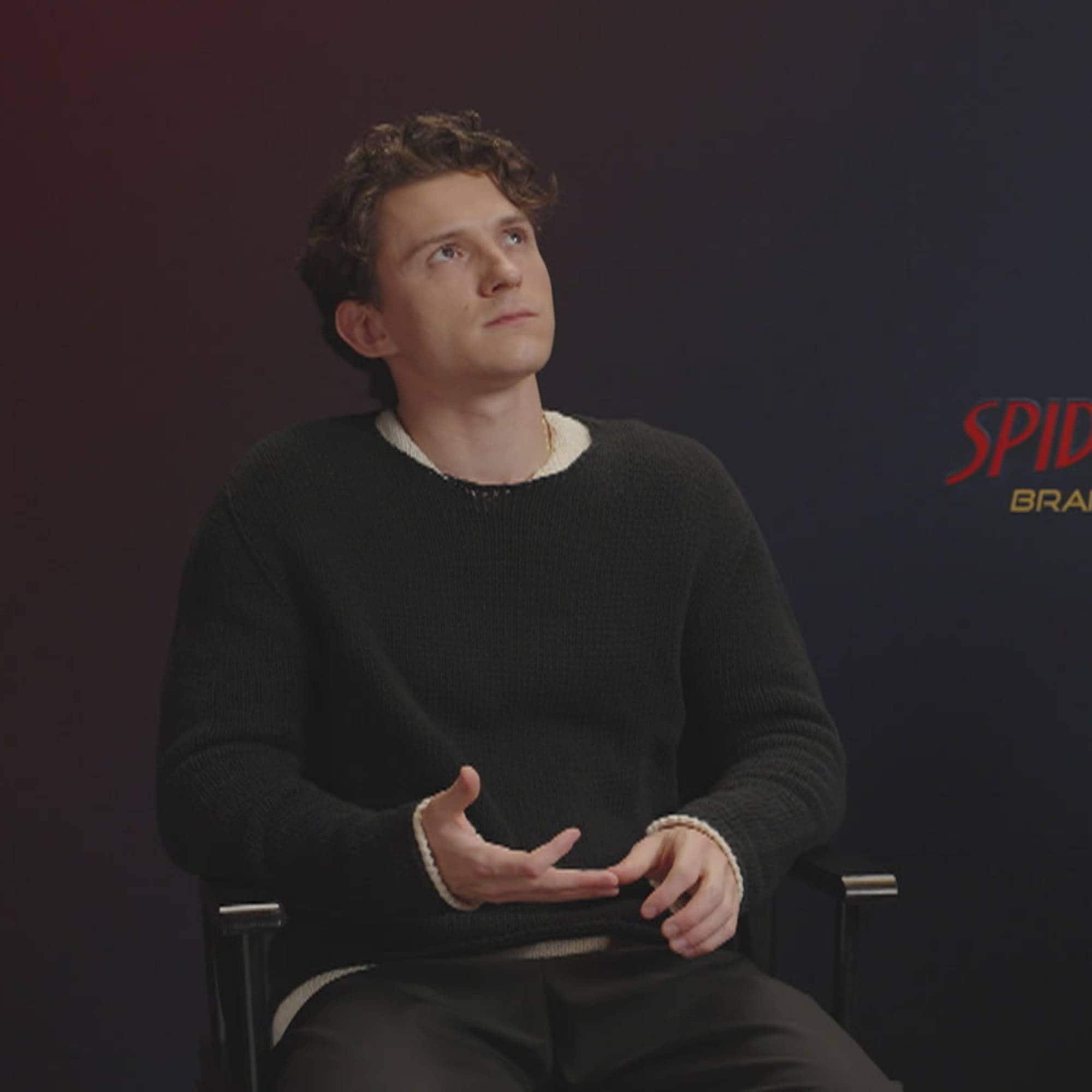 Skuespillerne Tom Holland og Zendaya sitter i hver sin stol foran en mørkeblå bakgrunn med «Spider-Man: Brand New Day»-logo. Holland har på seg en mørk genser og snakker mens han gestikulerer. Zendaya har på seg en mørk kjole med et spindelvev- og edderkoppmotiv over brystet. Mellom dem står et lite bord med drikke og en telefon. (Bildebeskrivelsen er laget av en KI-tjeneste)