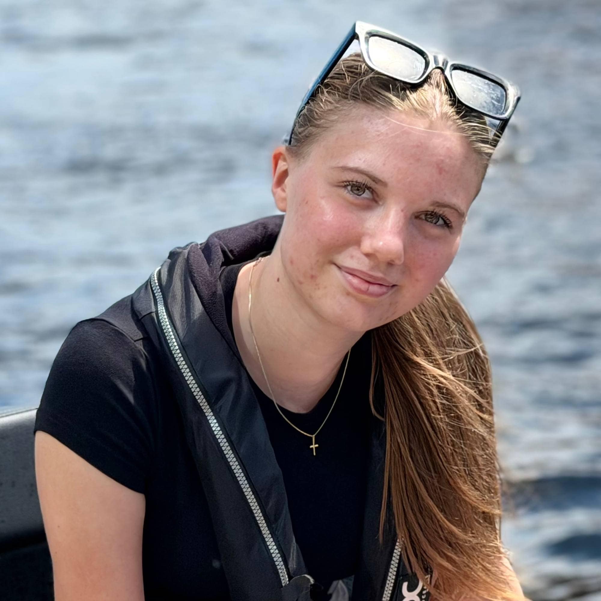 Ung jente med solbriller på hodet, brunt lang hår i en liten RIB. Ser sjø og påhengsmotor i bakgrunnen. 