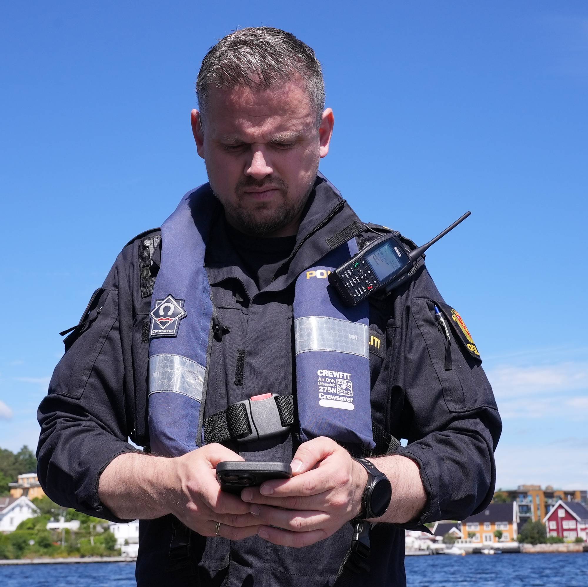 Båtfører på politibåten i Arendal ser ned i mobilen som han bruker til å skrive ut bøter. 