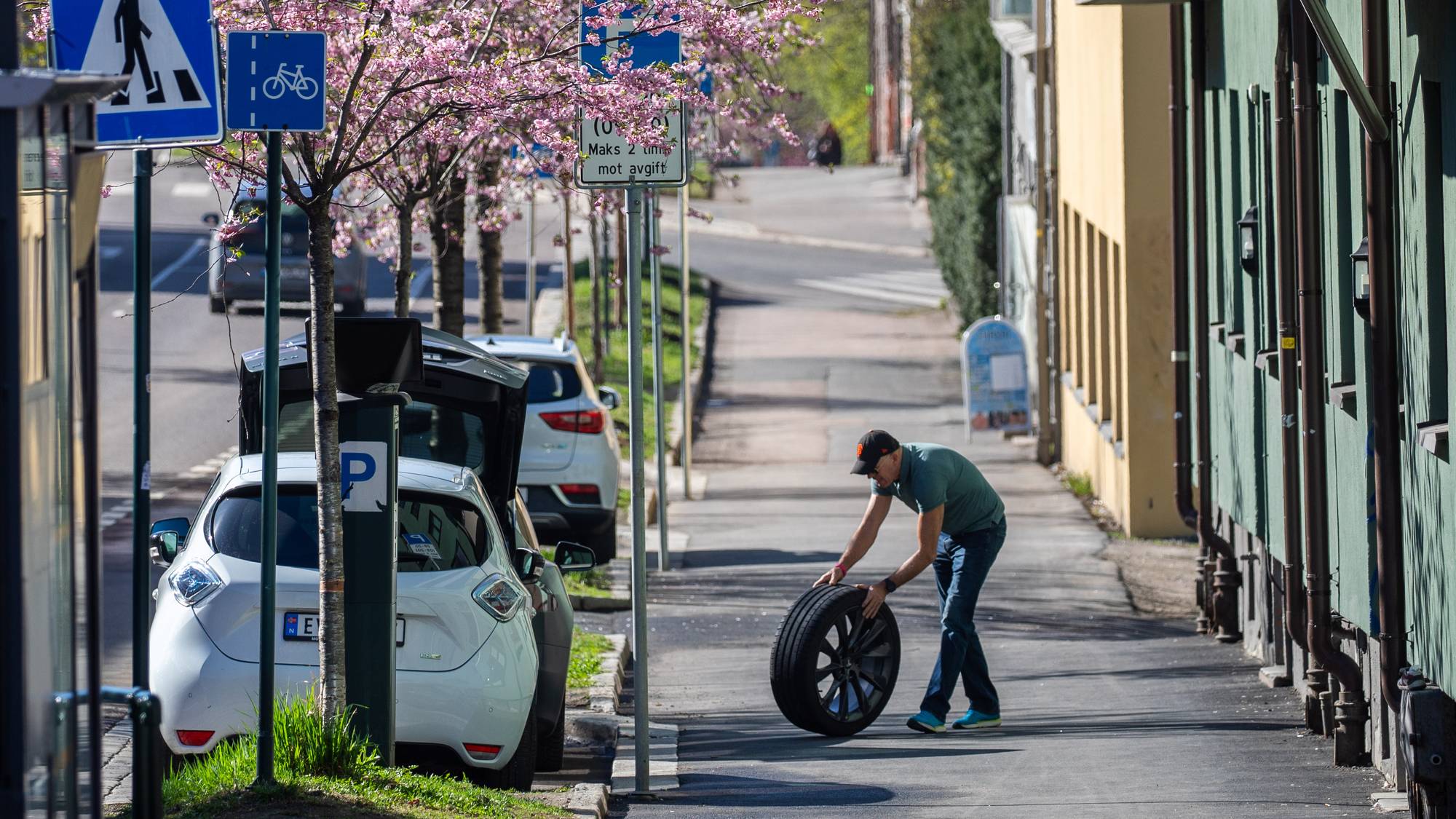 En mann ruller et dekk langs en gangvei i vårlig vær
