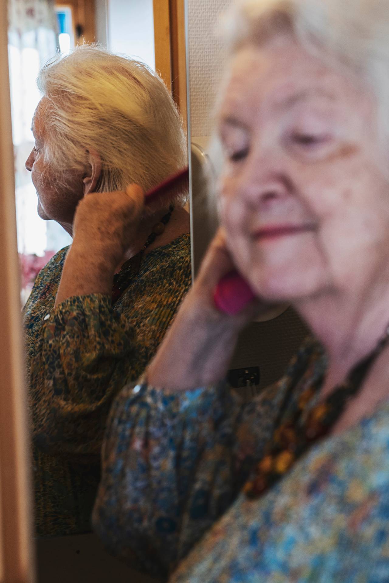 Anne Marie grer håret sitt mens hun ser seg i speilet. På veggen ved siden av henger noen tegninger hun har tegnet.