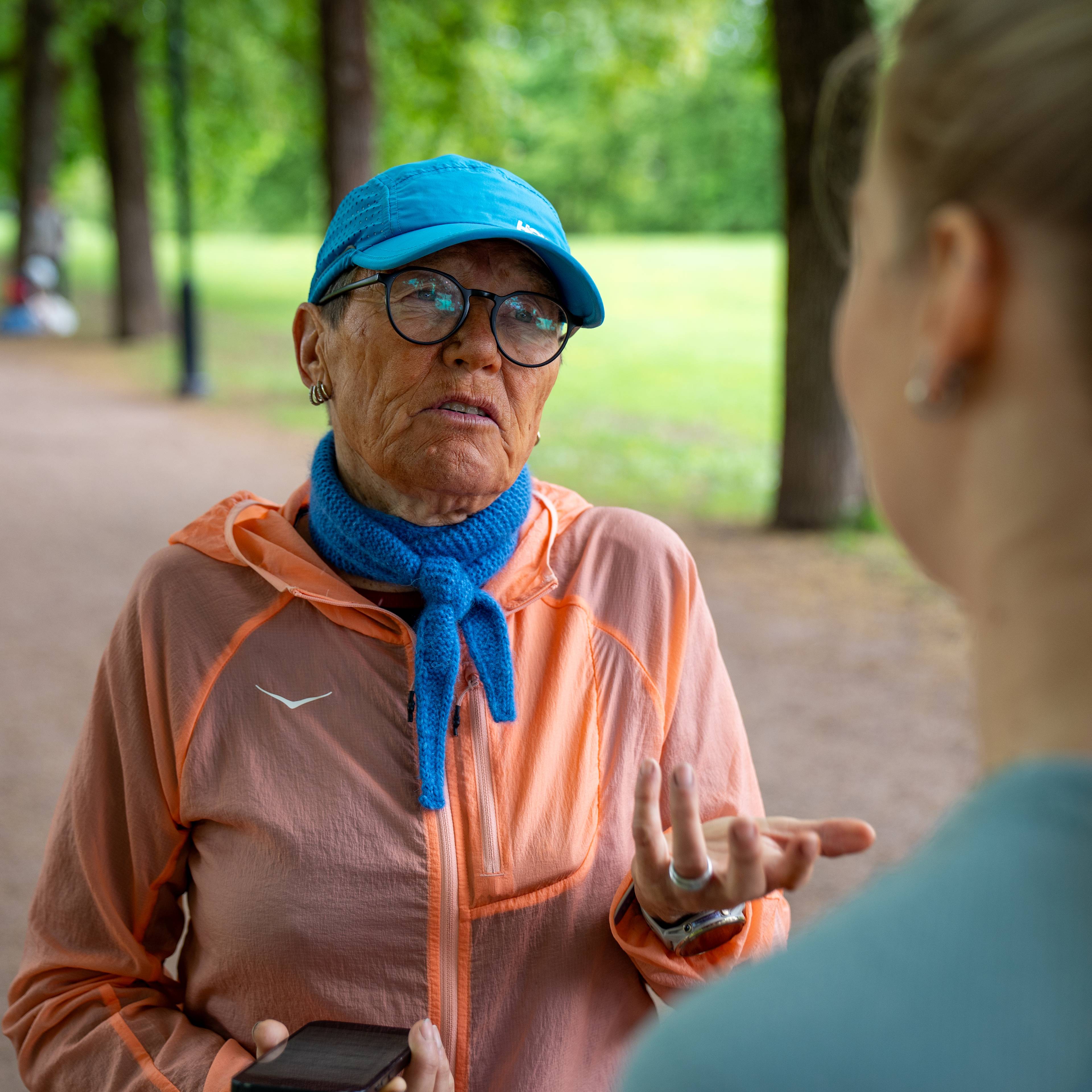 En kvinne ser på en annen kvinne. De har begge på løpeklær. Den ene kvinner lærer opp den andre i løping. De er utenførs i en park.