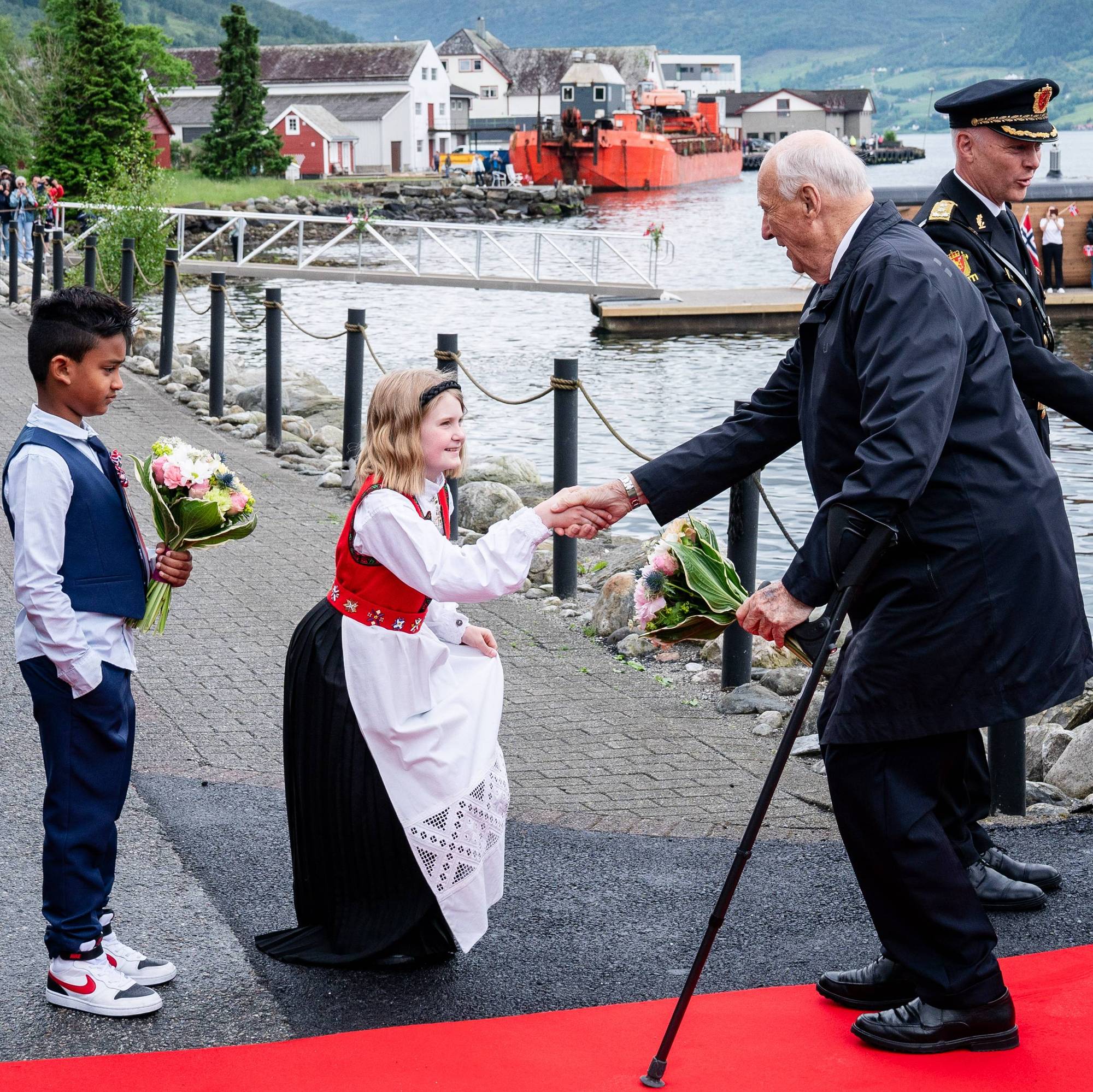 Kong Harald hilser på en blomsterjente som neier, under kongeparets fylkestur i Agder og Rogaland i 2024