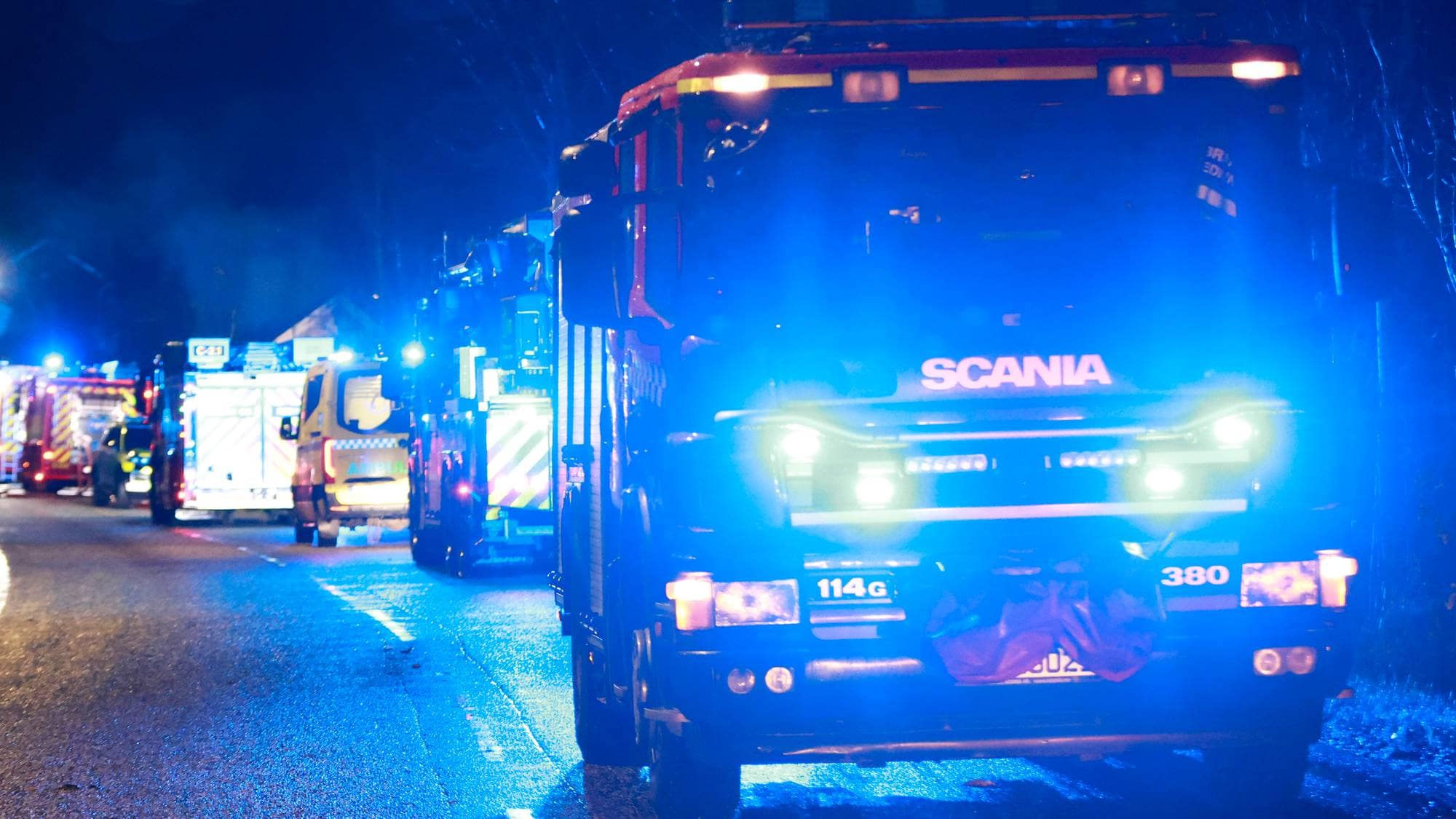 Mange brannbiler og andre nødetater på stedet. Mørkt ute og blålys synlig.